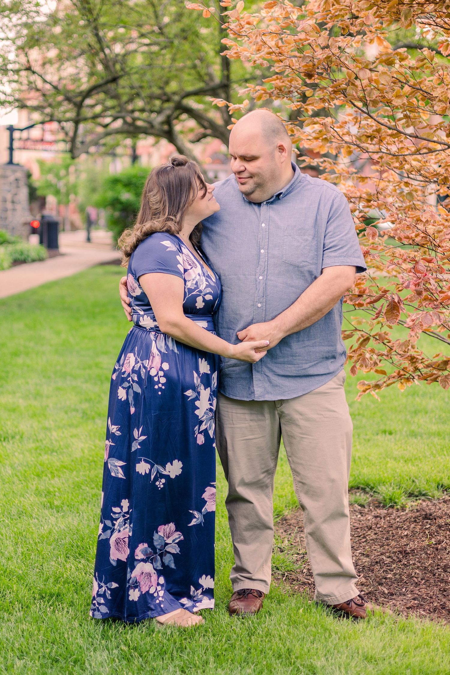 A couple shares an intimate moment in a garden setting, with the woman wearing a floral navy dress and man in gray shirt.