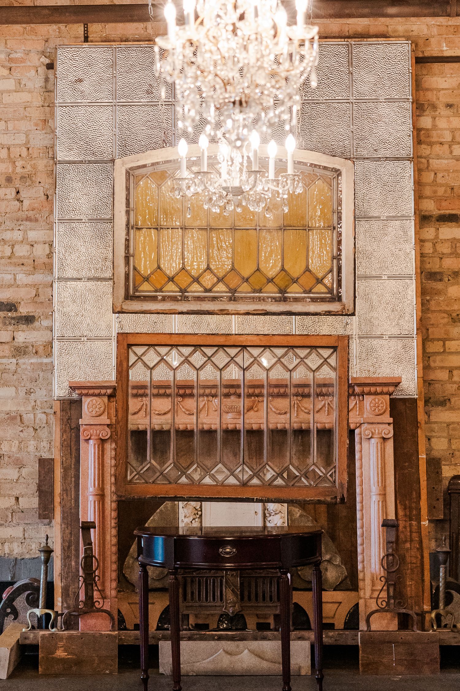 Elegant crystal chandelier hangs above an ornate wooden frame with decorative stained glass in a vintage interior.