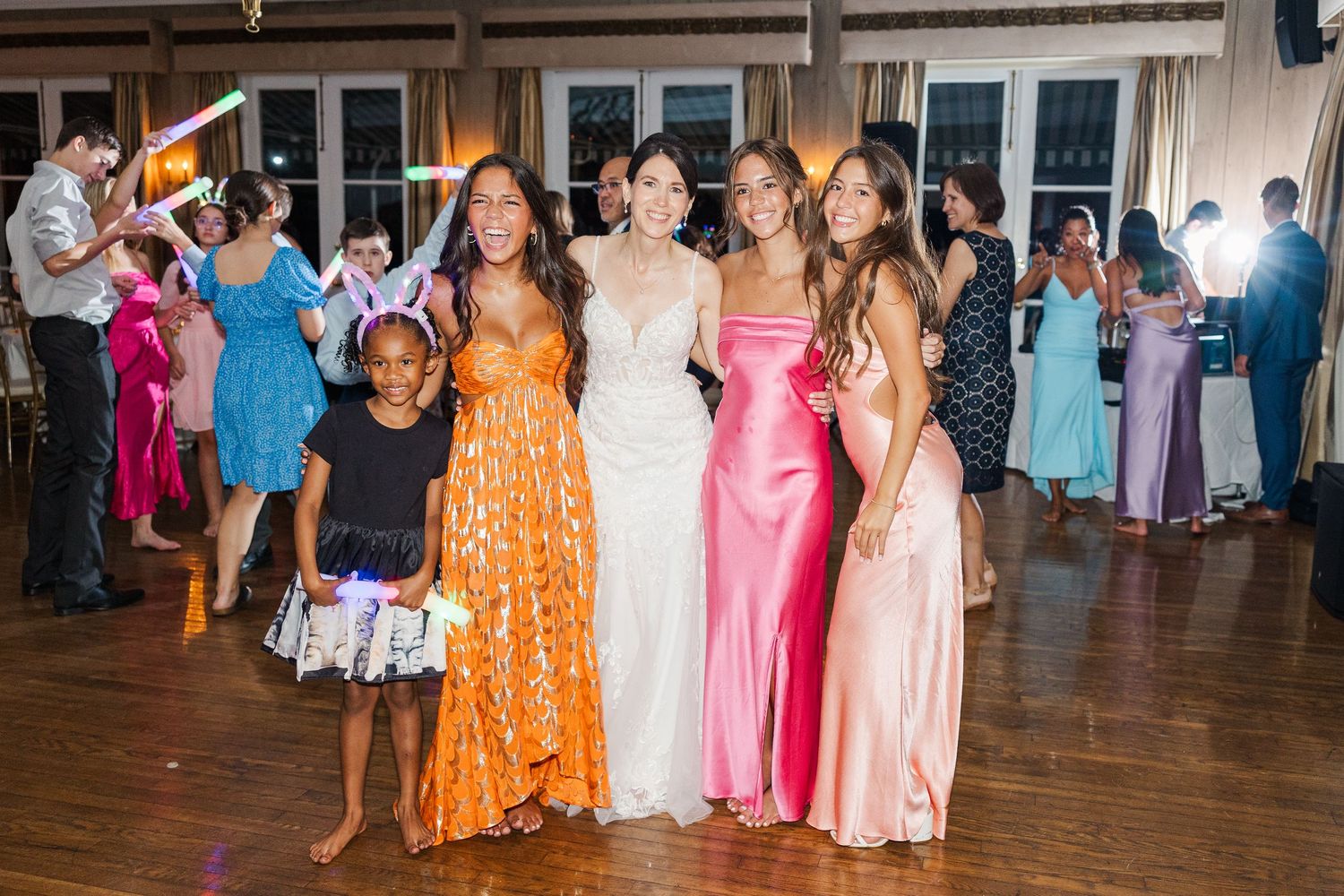 Wedding party poses together on a dance floor wearing vibrant colorful formal dresses.