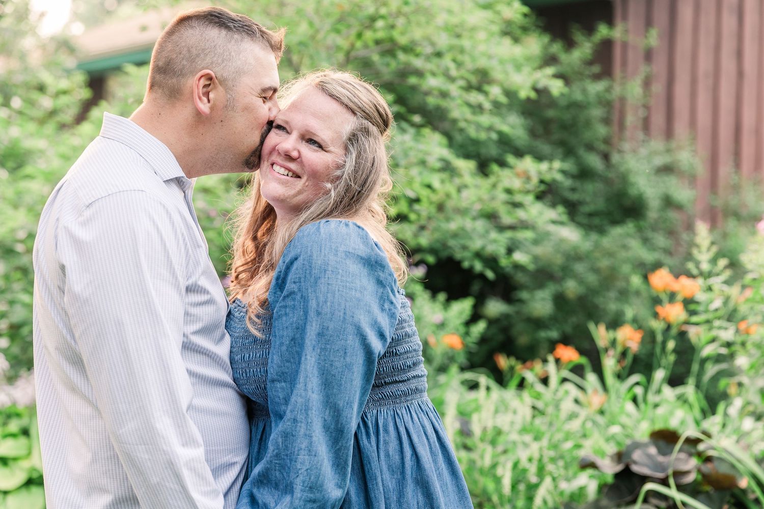 Couple sharing a tender moment in casual wear surrounded by garden greenery.