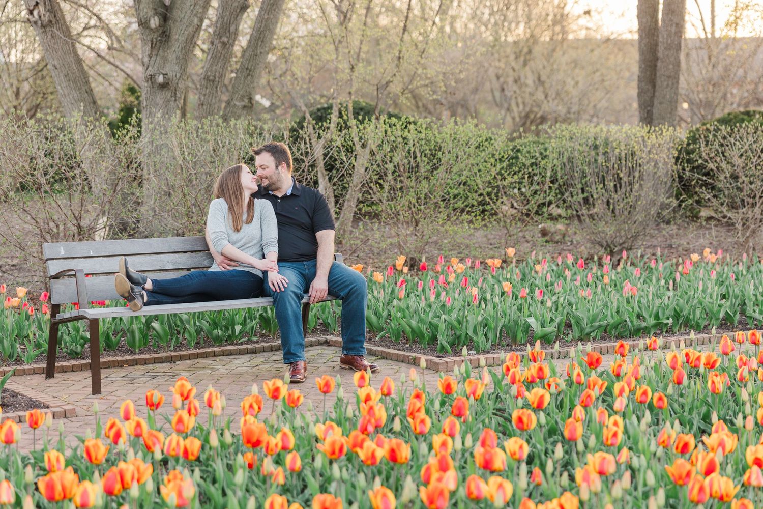 Couple sitting on bench surrounded by blooming orange tulips in garden setting.