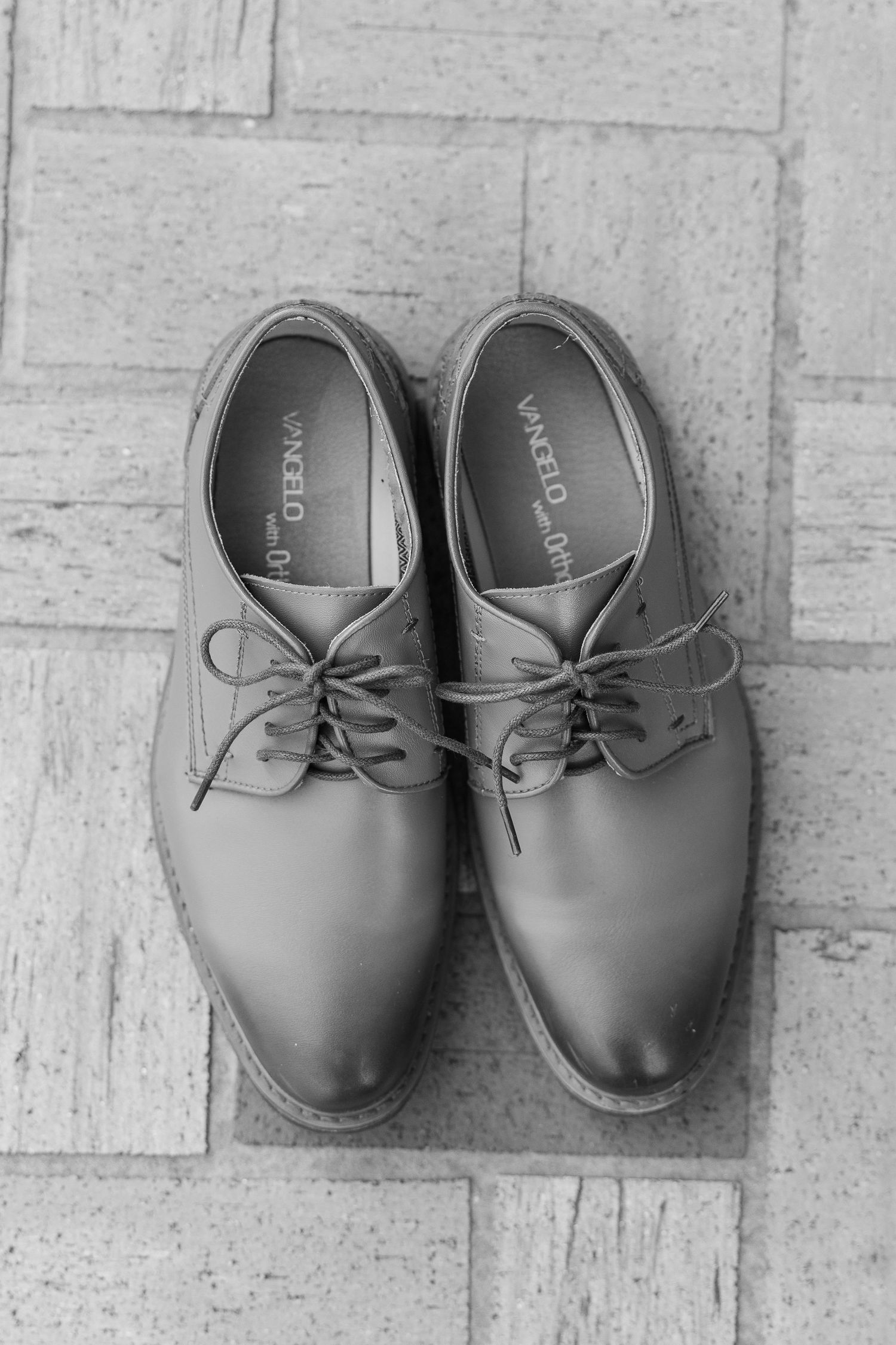 Classic grey leather oxford dress shoes displayed on stone tile floor.
