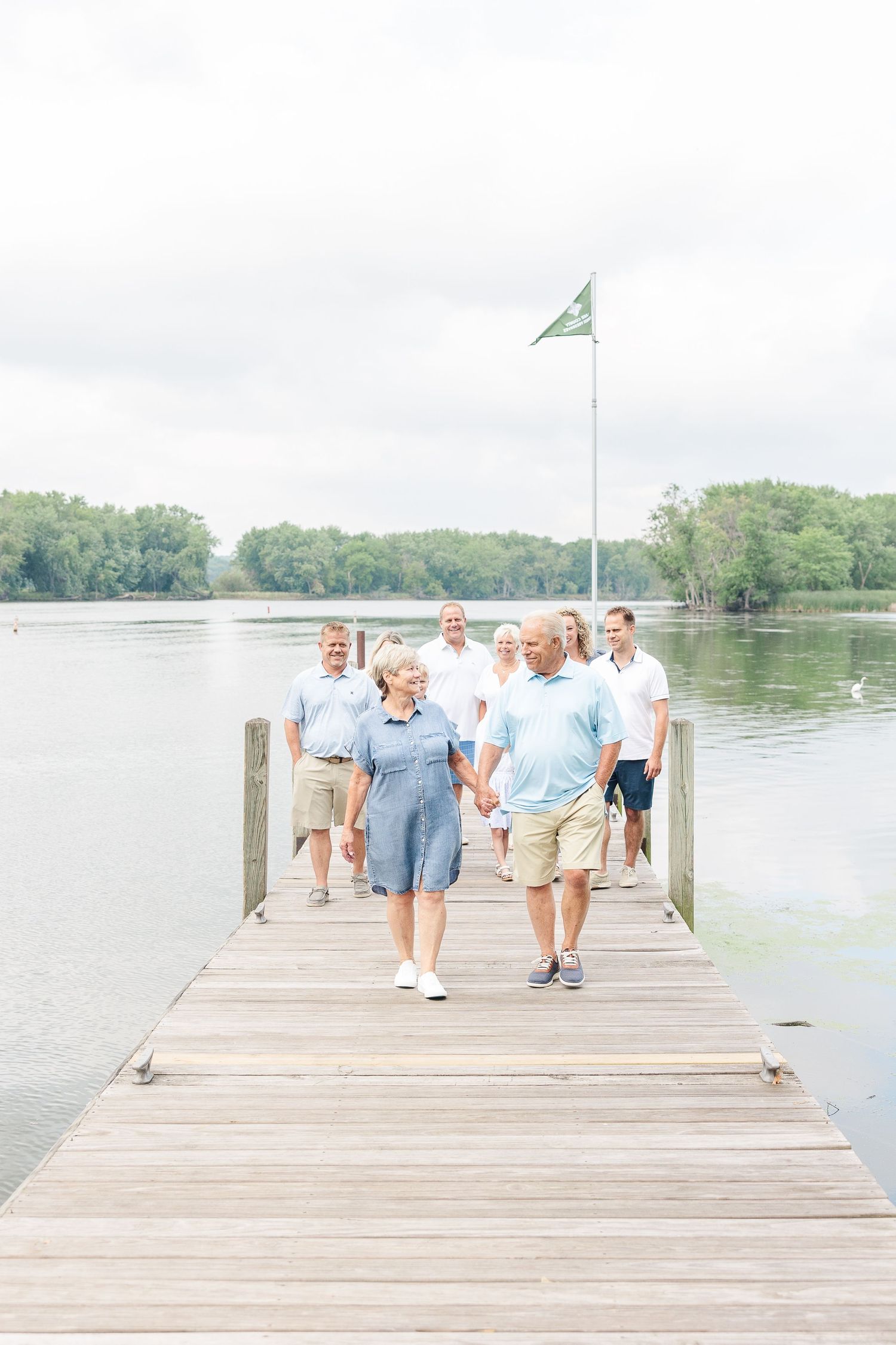 A group walks together on a wooden pier overlooking a serene lake with trees in the background.