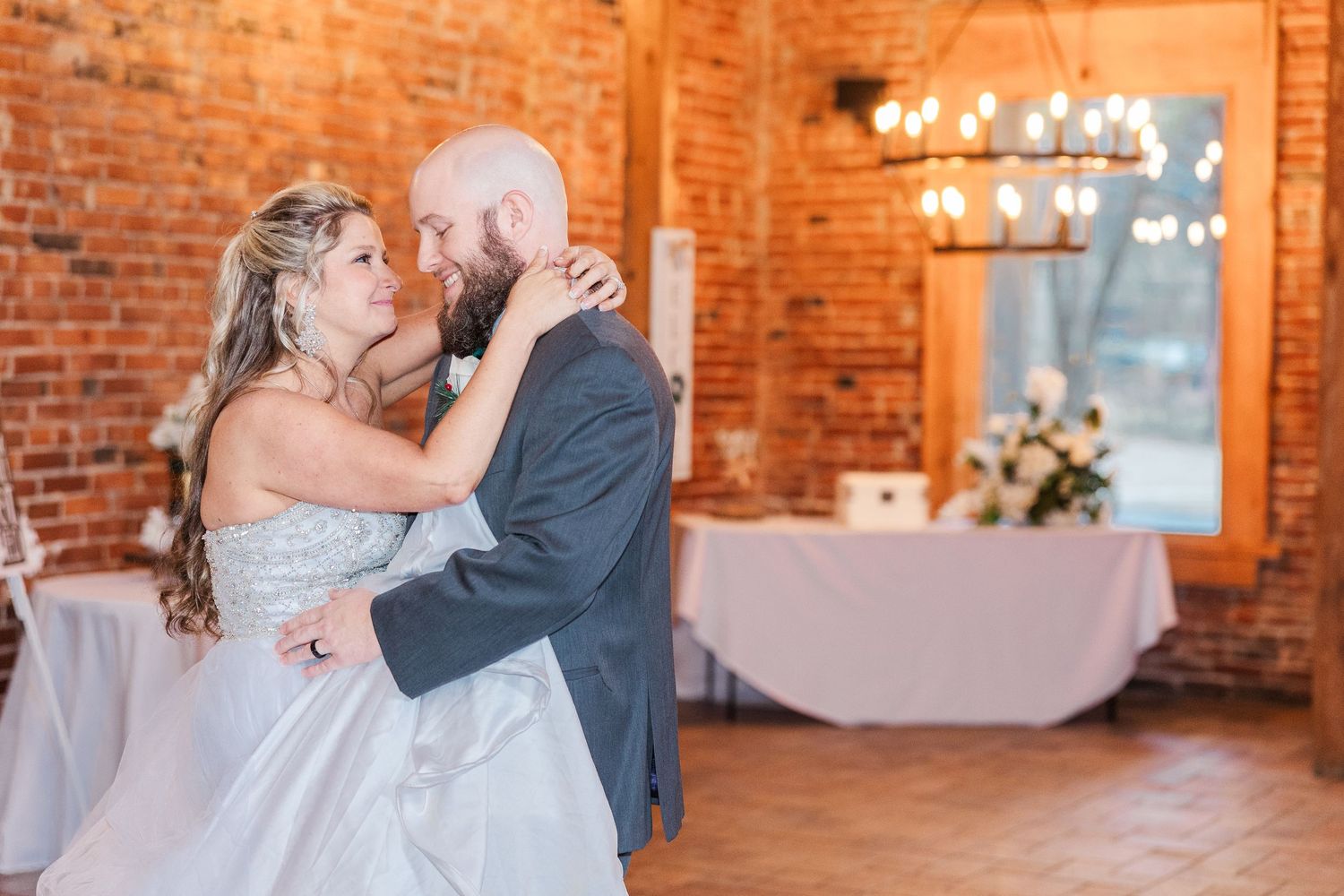 Couple dancing in rustic brick venue with chandelier and romantic lighting.