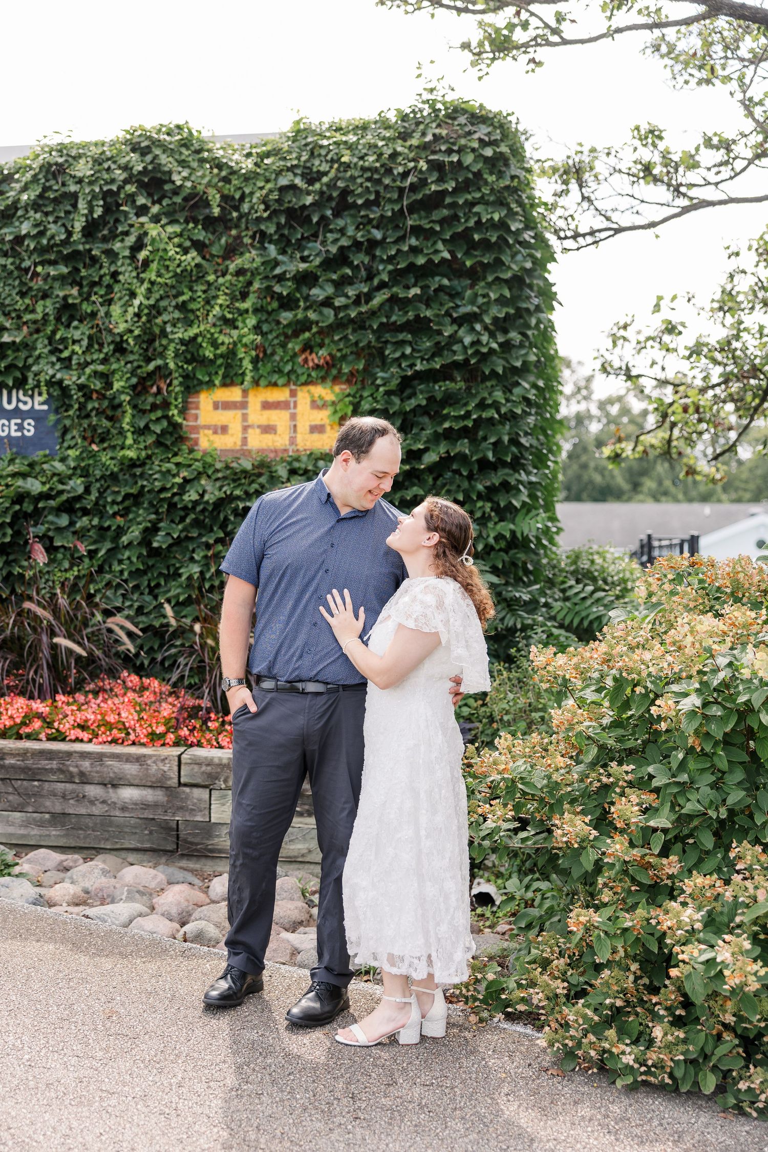 Happy couple sharing a romantic moment outdoors near an ivy-covered wall with yellow sign and lush greenery.