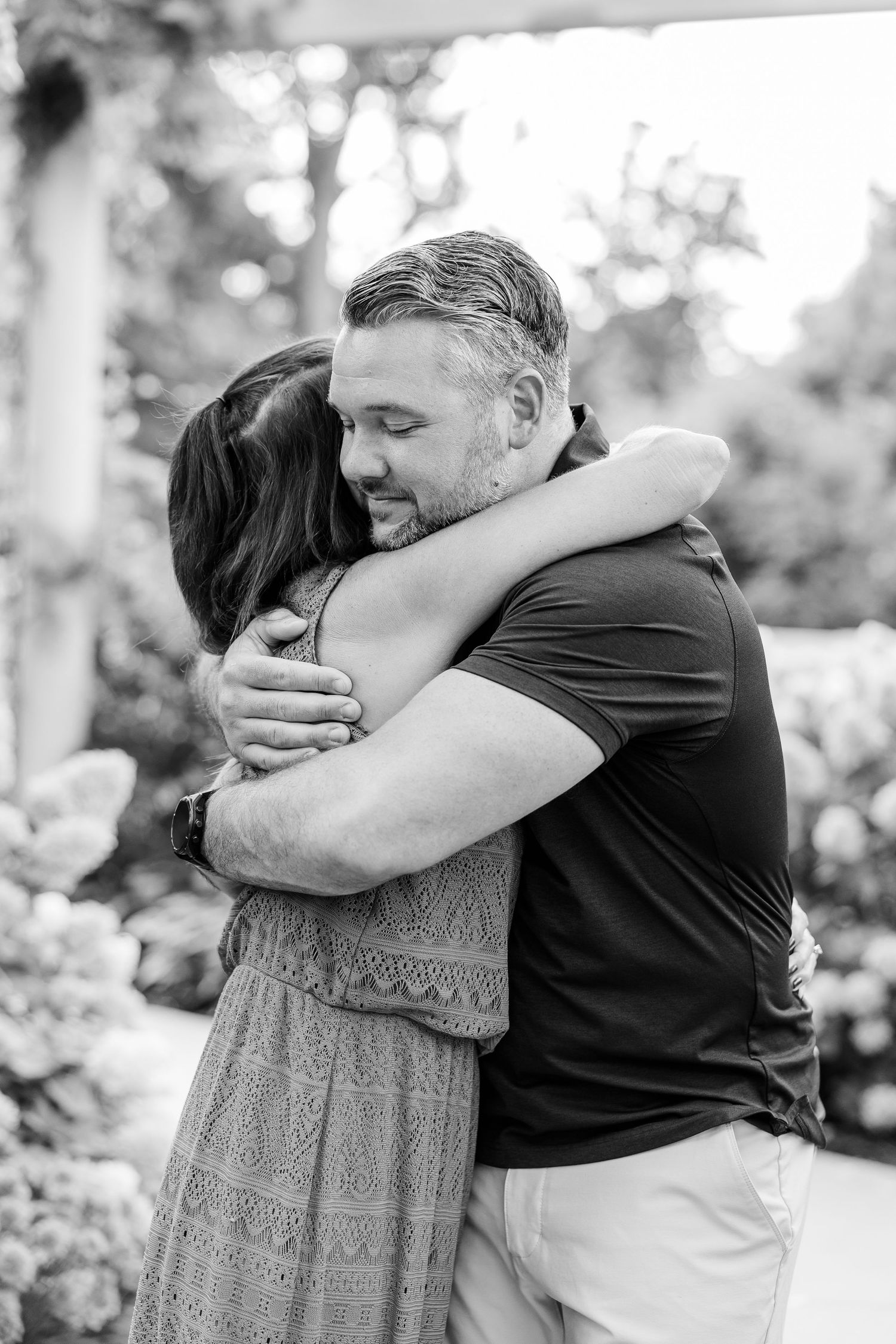 Black and white photo of couple sharing a warm embrace in garden.