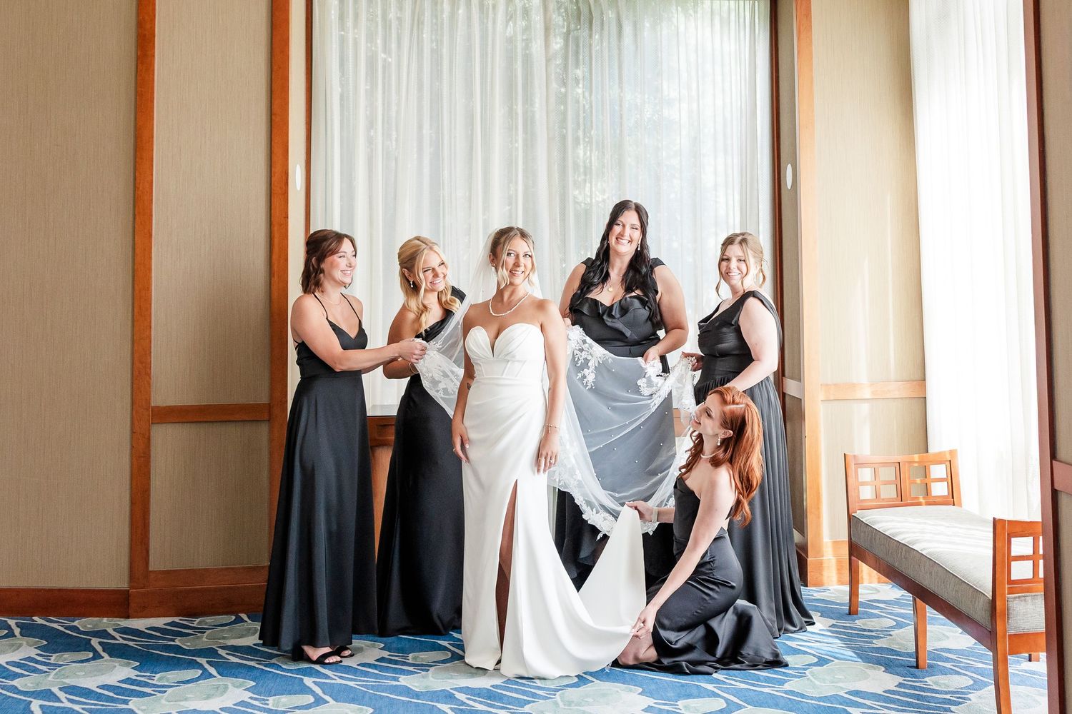 Bride in white gown surrounded by bridesmaids in black dresses helping arrange her wedding dress train.