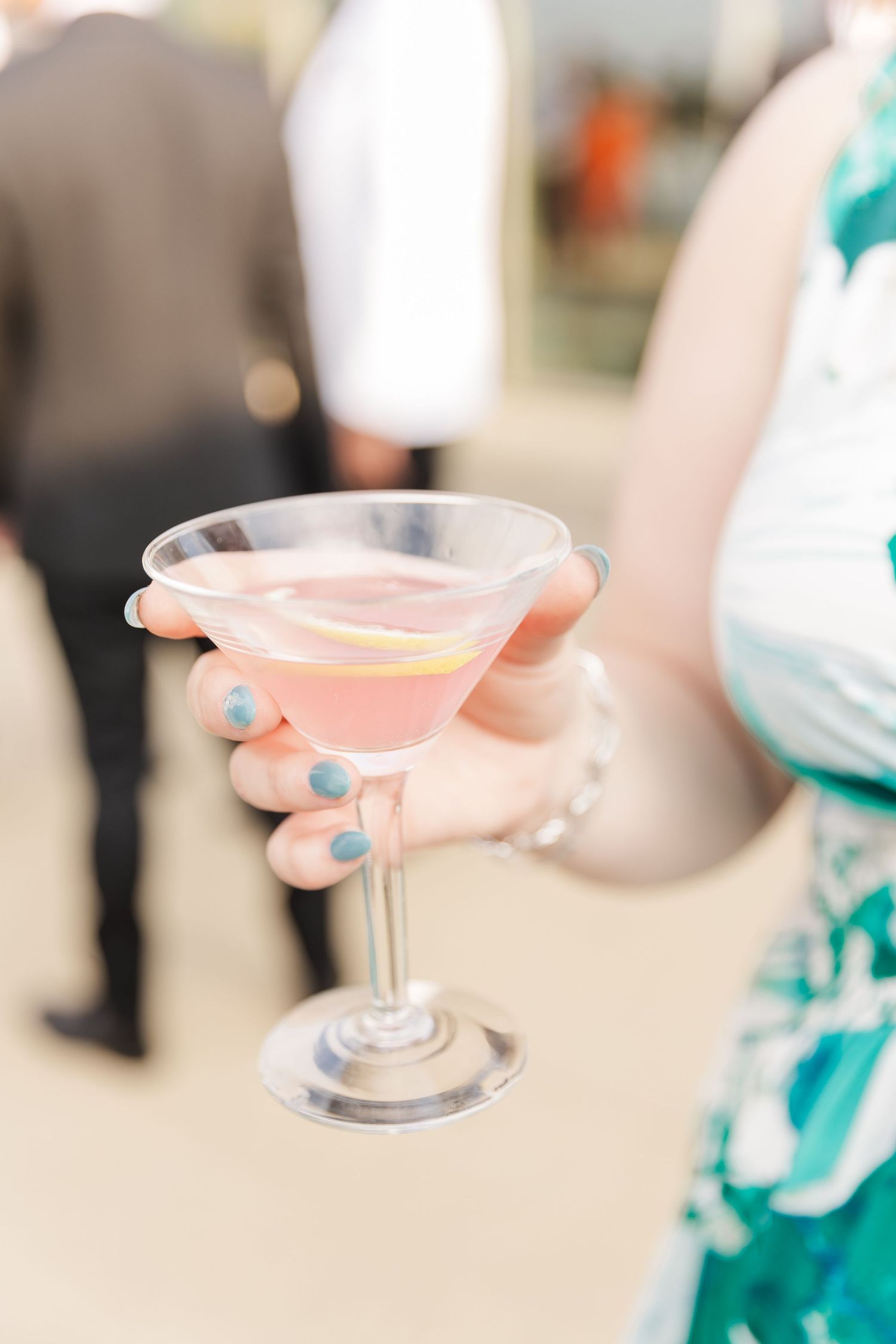 Hand holding a pink martini cocktail with lemon garnish at a wedding reception.