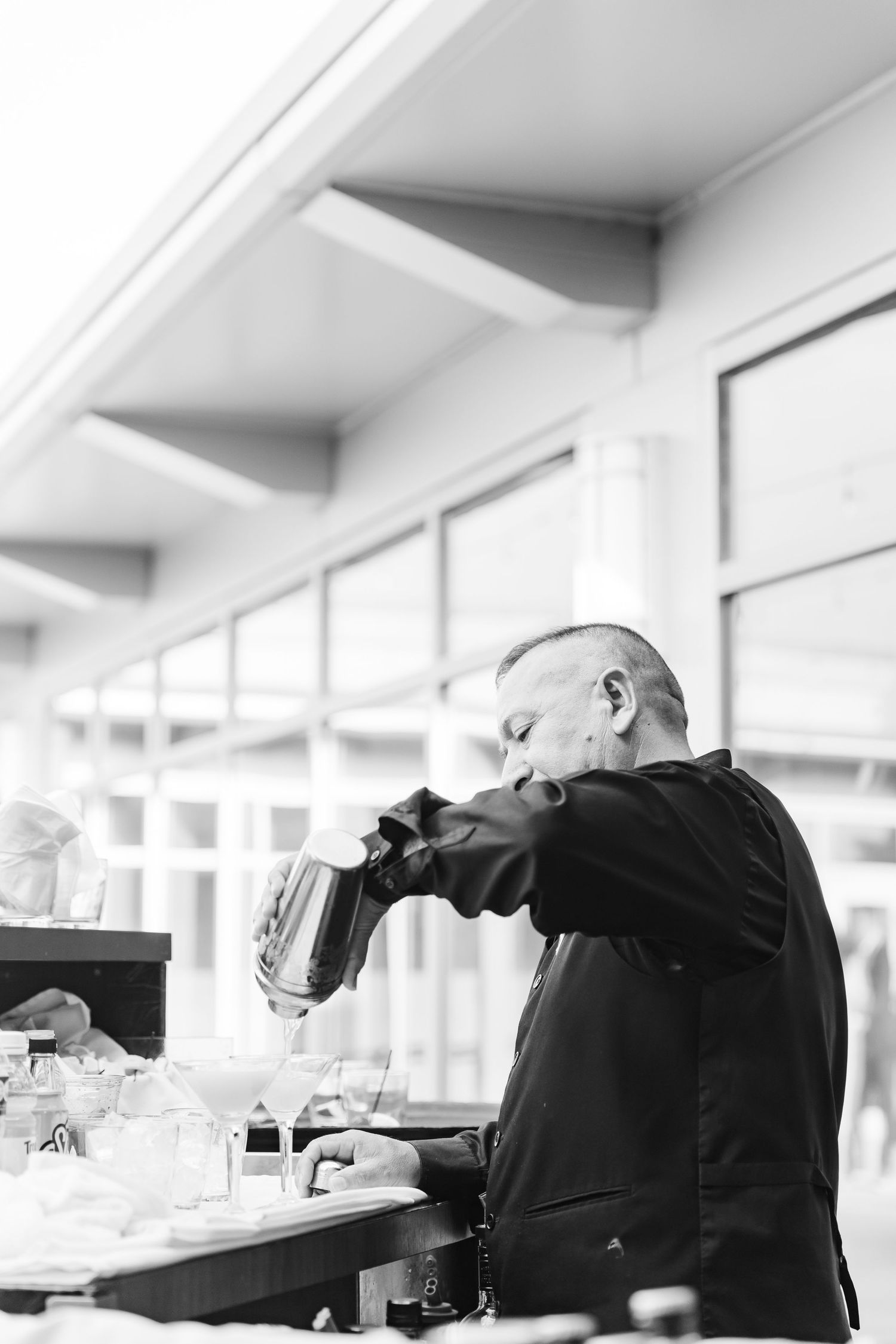Black and white photo of bartender pouring drinks at outdoor wedding reception bar service.