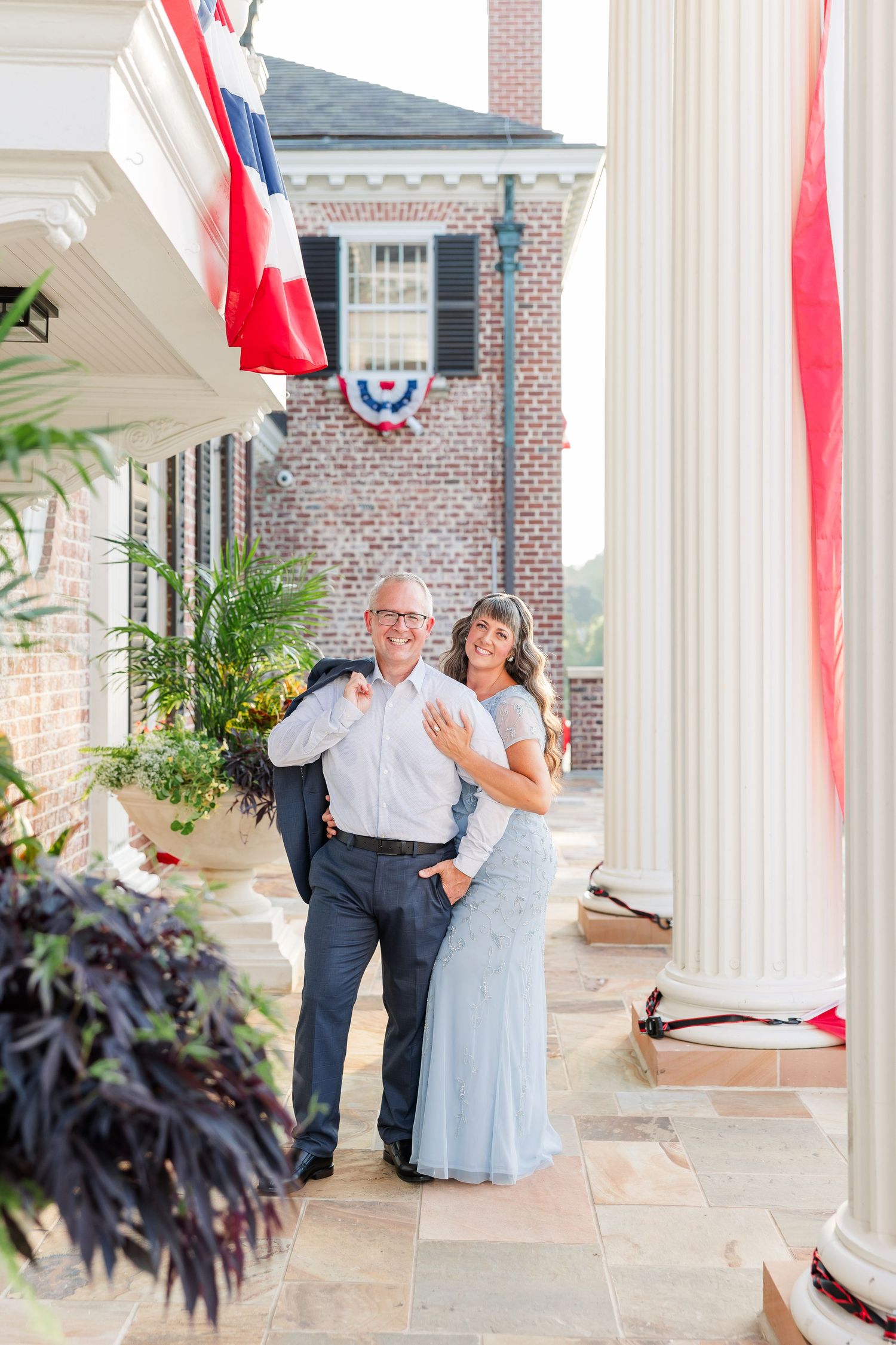 Couple smiling together on a brick building porch with patriotic bunting decorations and white columns.