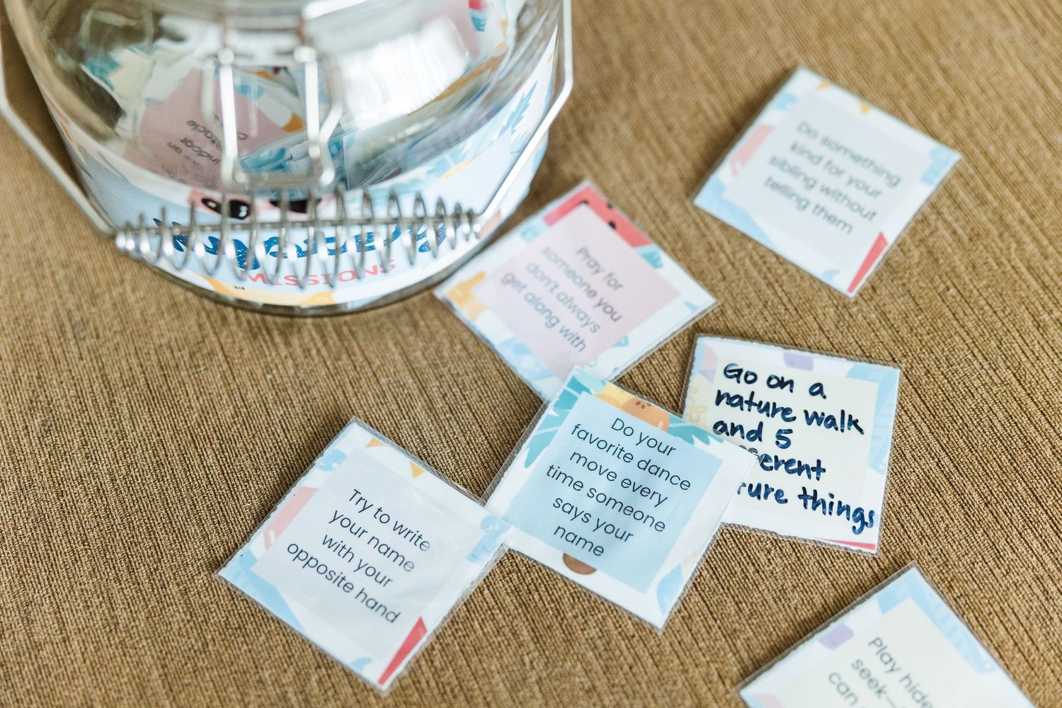 Mystery Mission cards spread out beside a glass jar for kids summer activities