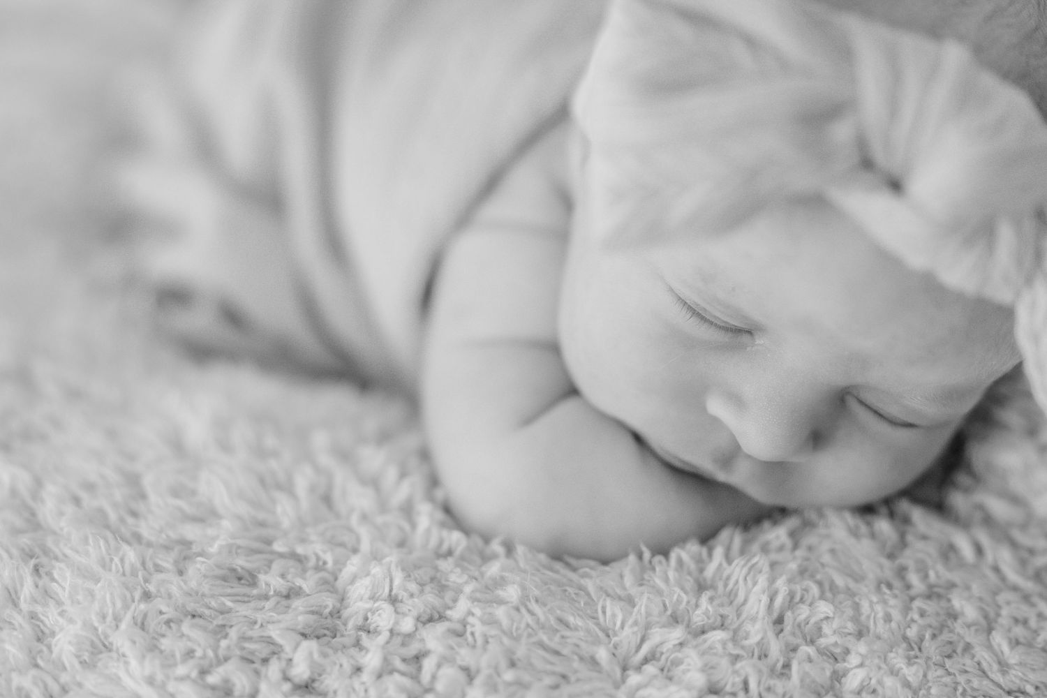 Peaceful newborn baby sleeping on fluffy white blanket, black and white photography.