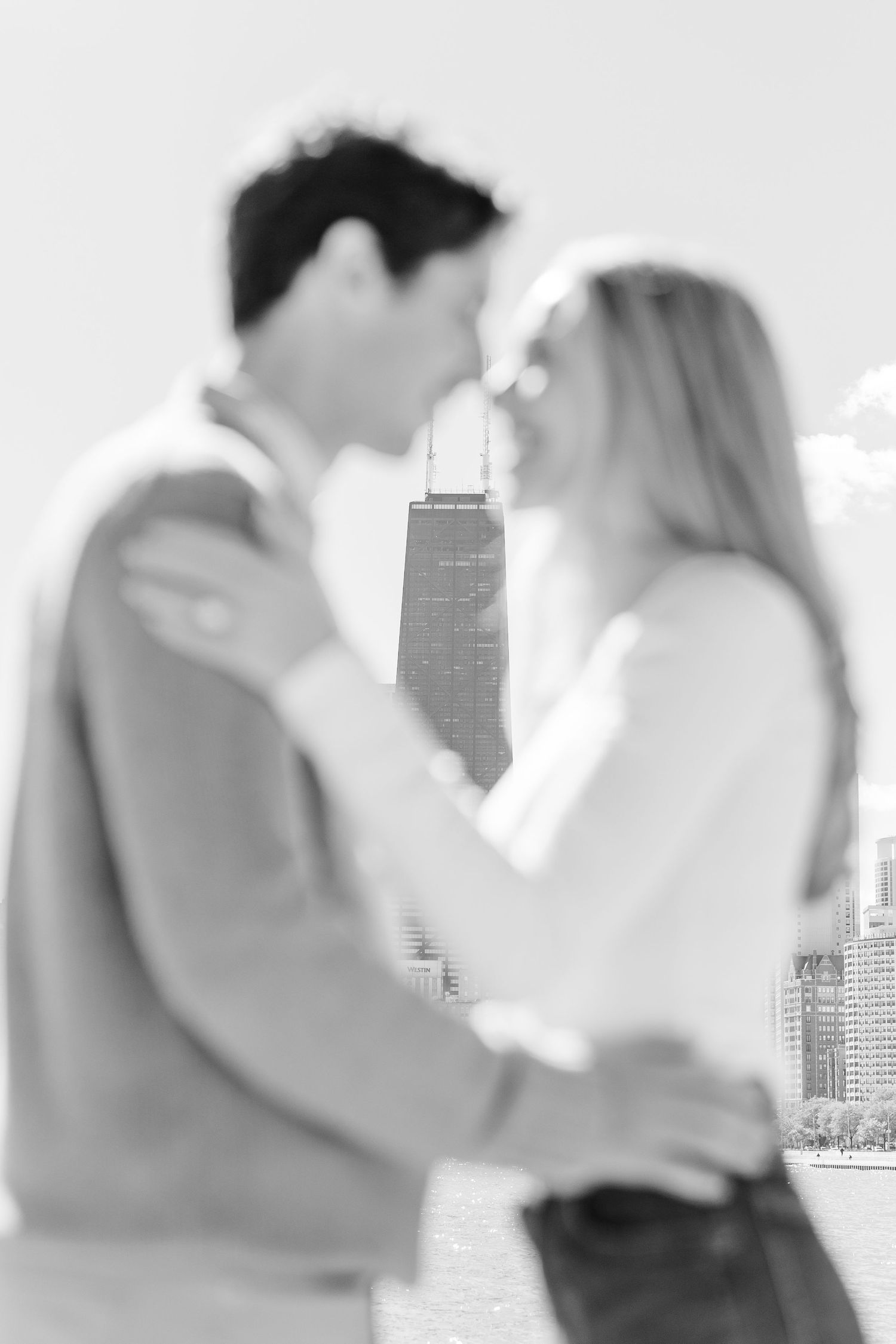 Soft-focus black and white photo of couple kissing with iconic Chicago Willis Tower in the background.
