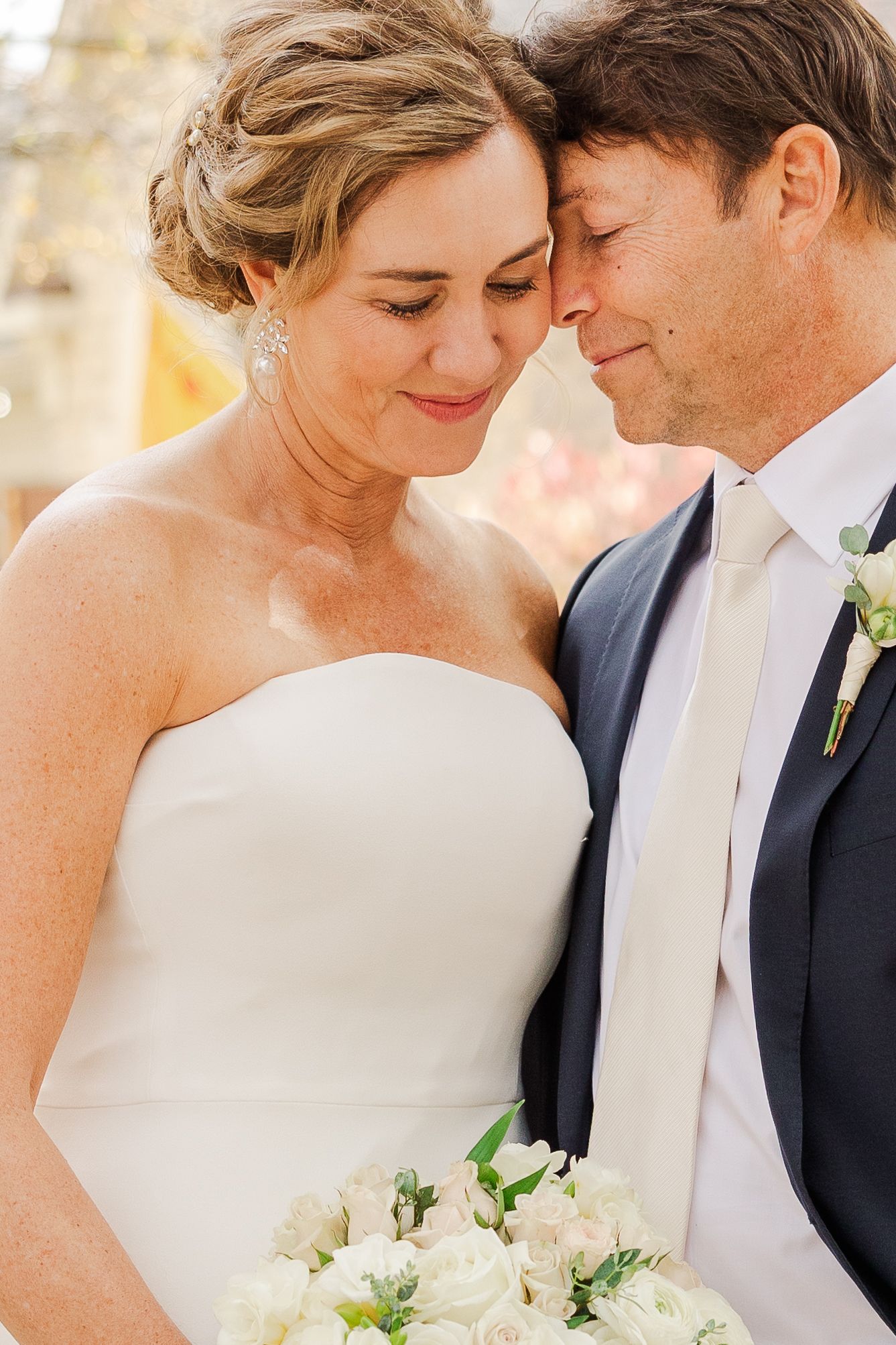 An intimate wedding portrait showing a tender moment with white floral bouquet.