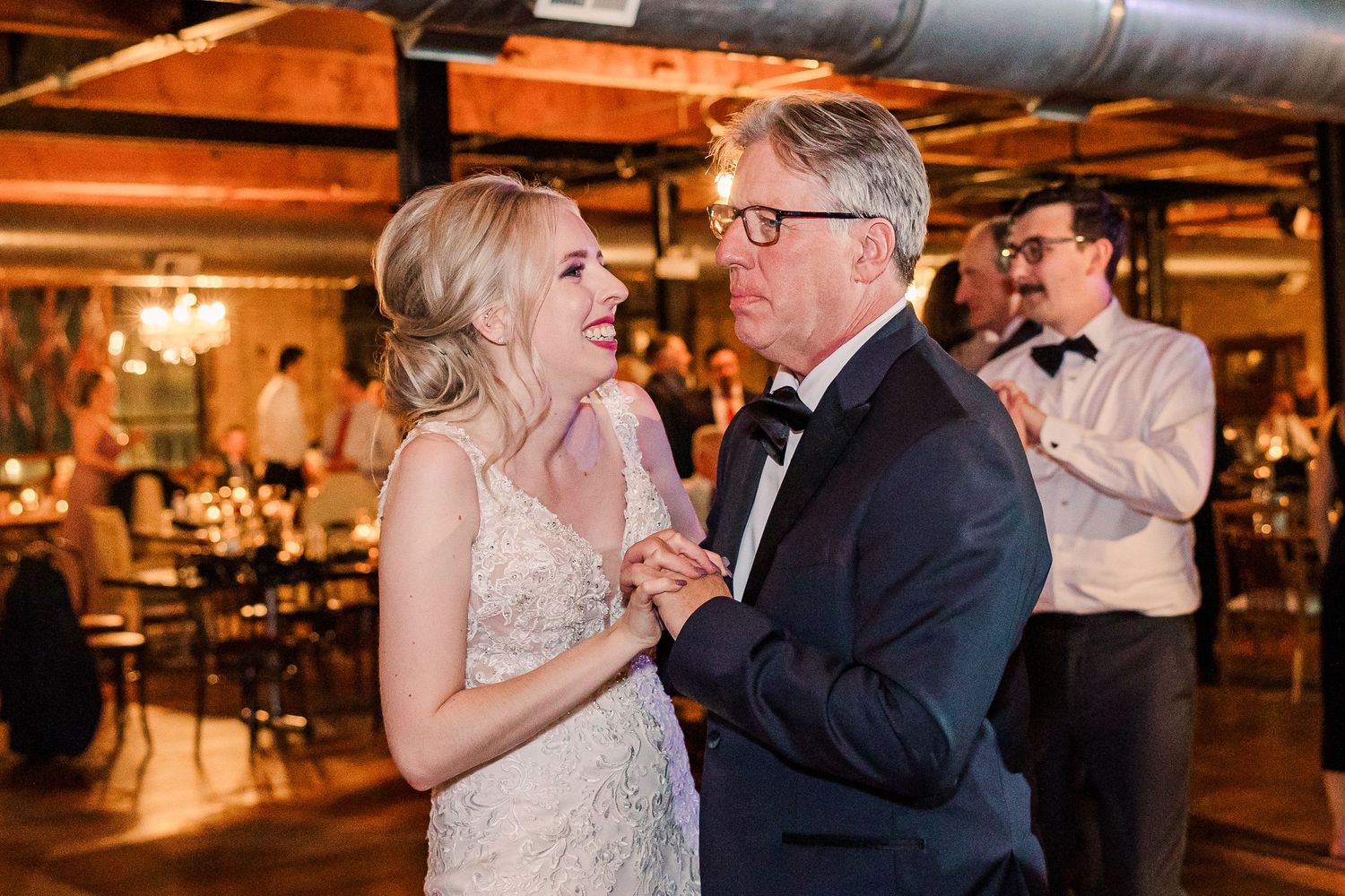 A joyful dancing moment captured in a rustic reception venue with exposed brick and ductwork.