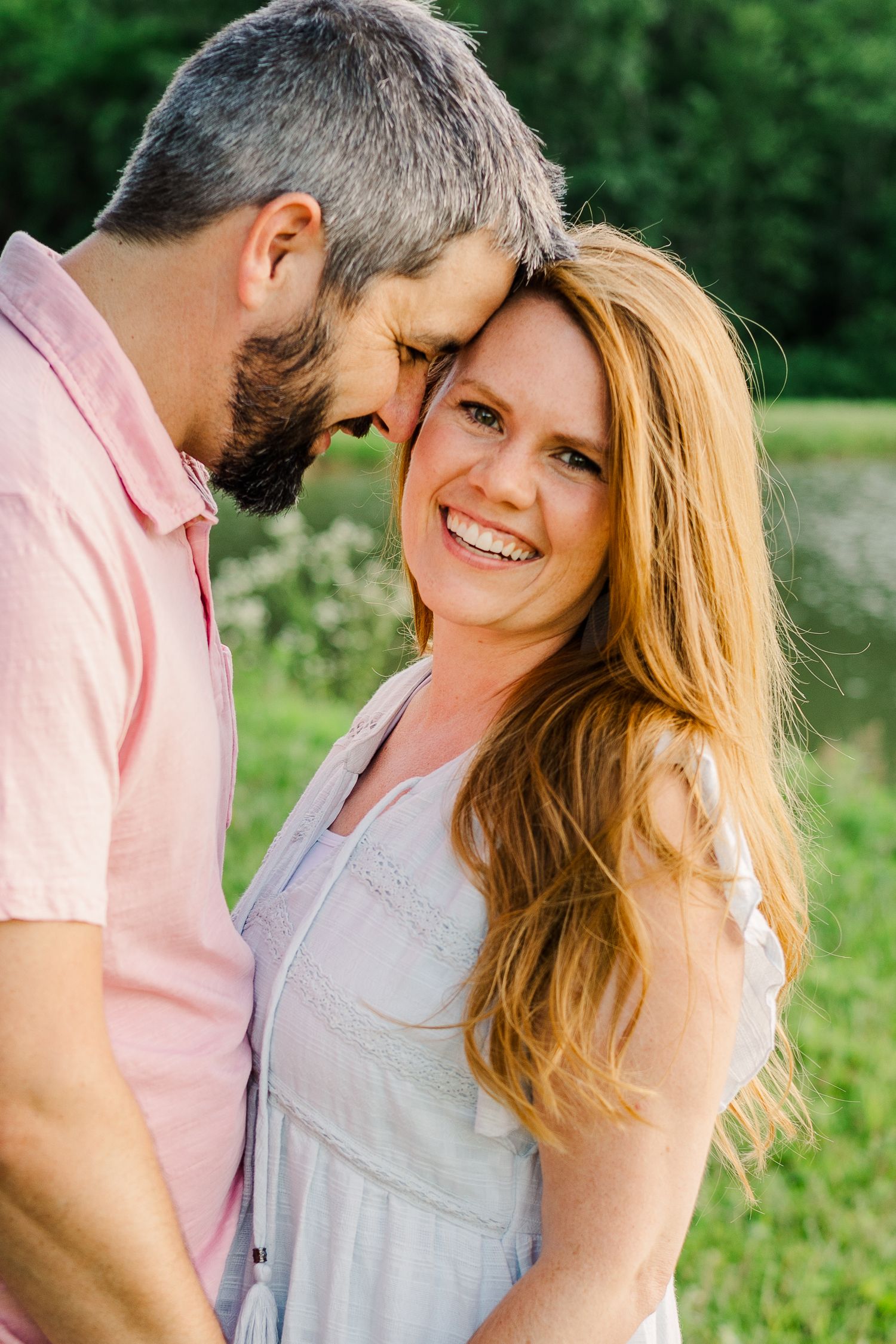 A romantic couple shares an intimate moment while smiling in a sunny outdoor setting.