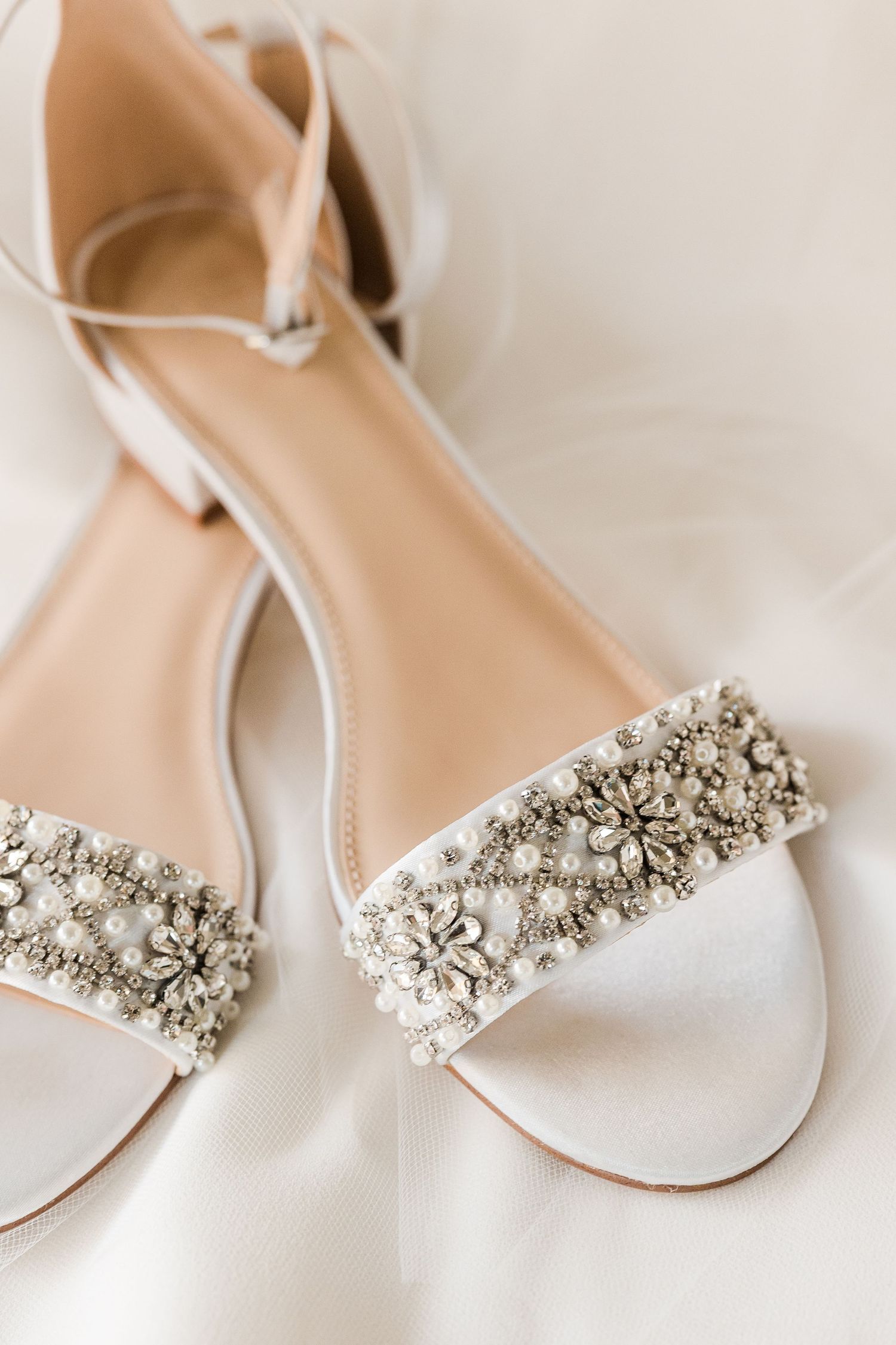 White bridal sandals with crystal embellishments on a soft white background.
