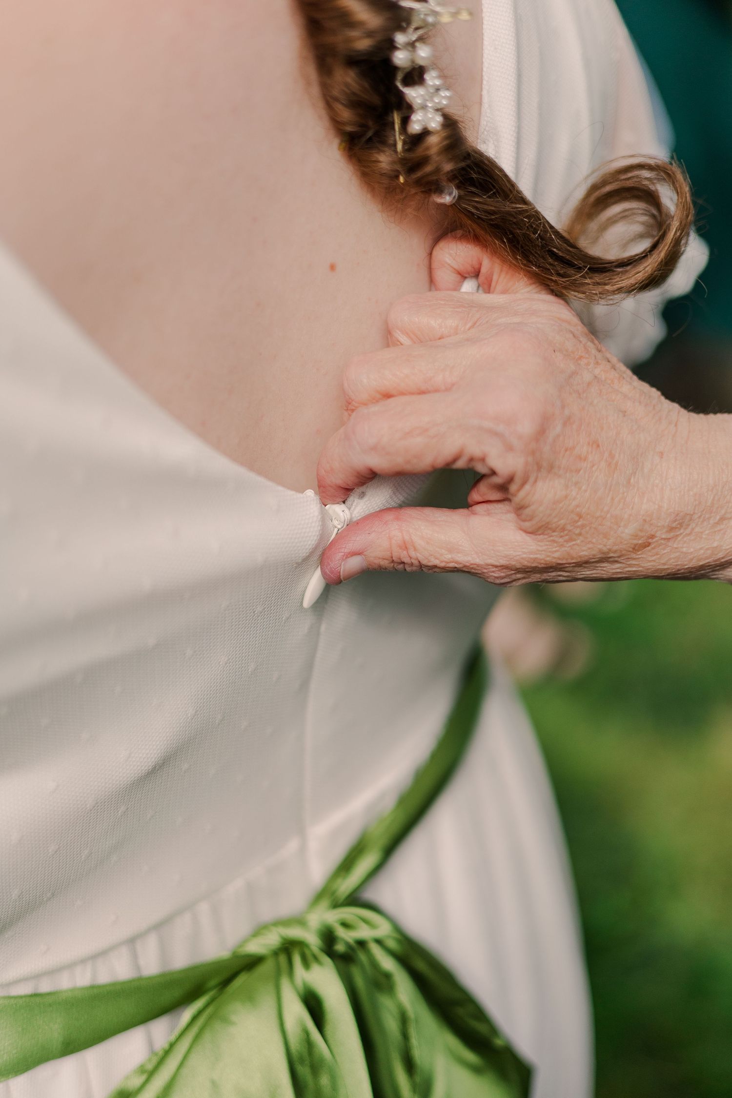Close-up detail of someone adjusting a white wedding dress with a green sash.