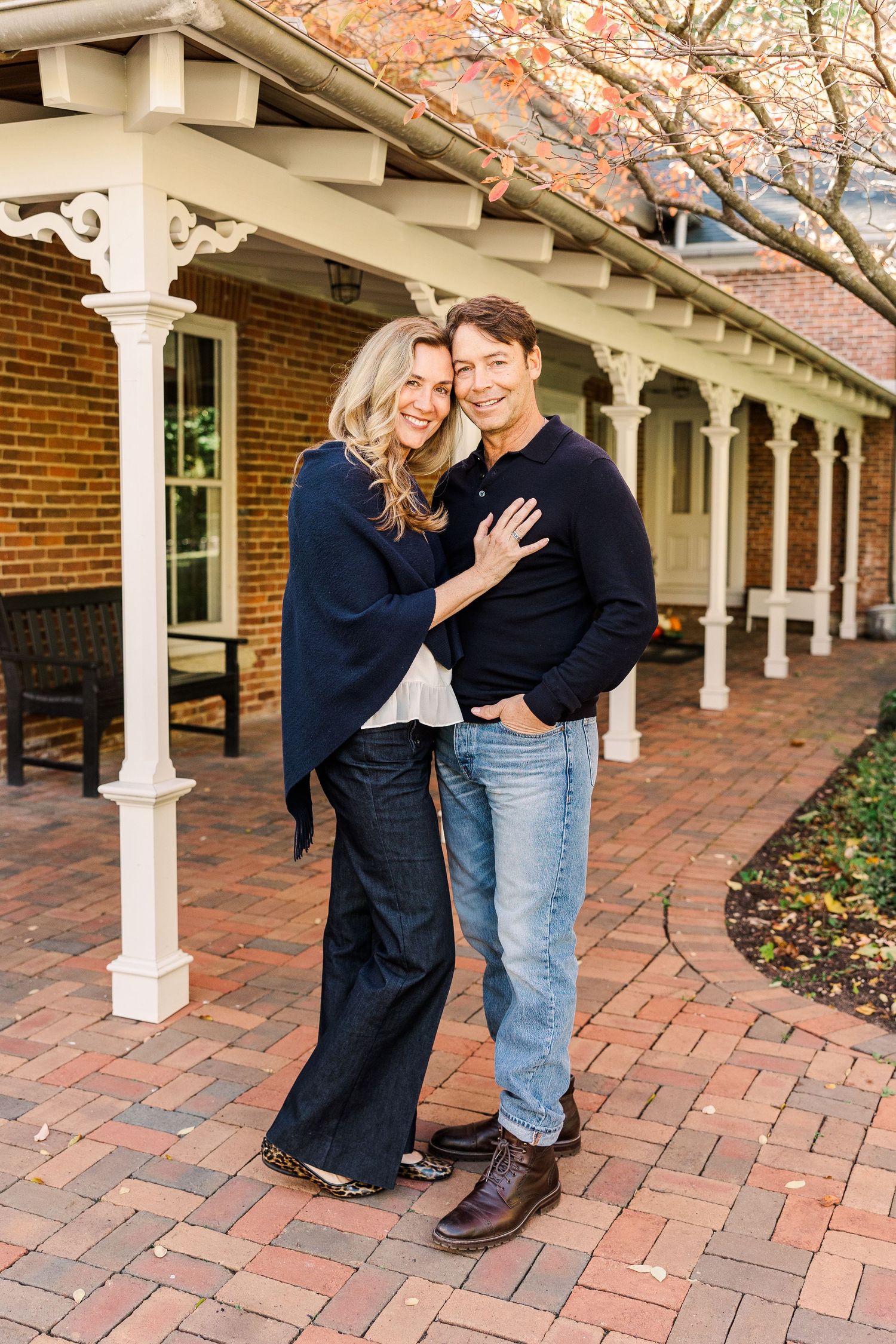 A couple embraces on a brick patio beneath a covered colonial-style porch.