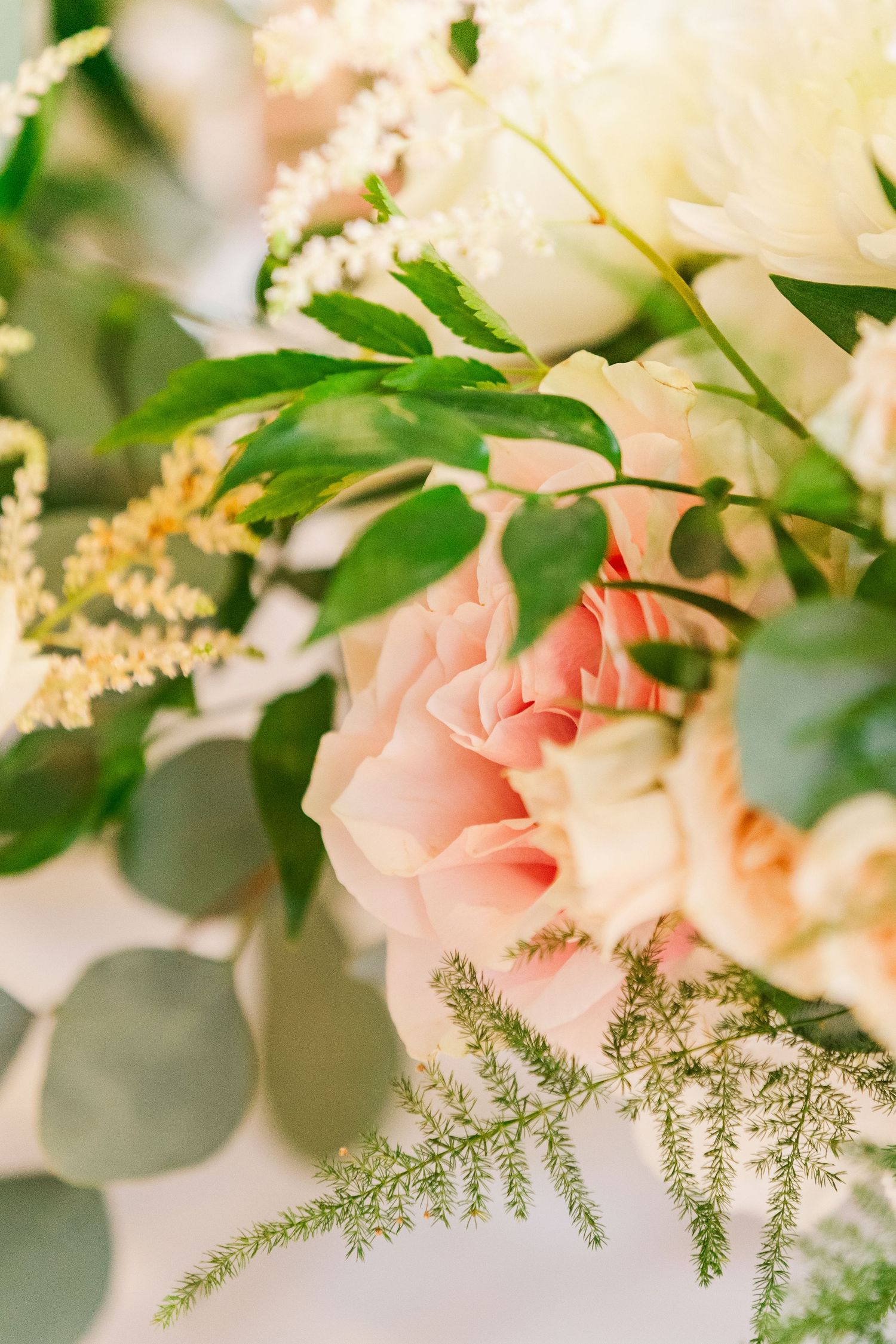 Close-up of delicate pink roses and white flowers with green foliage in romantic wedding arrangement.