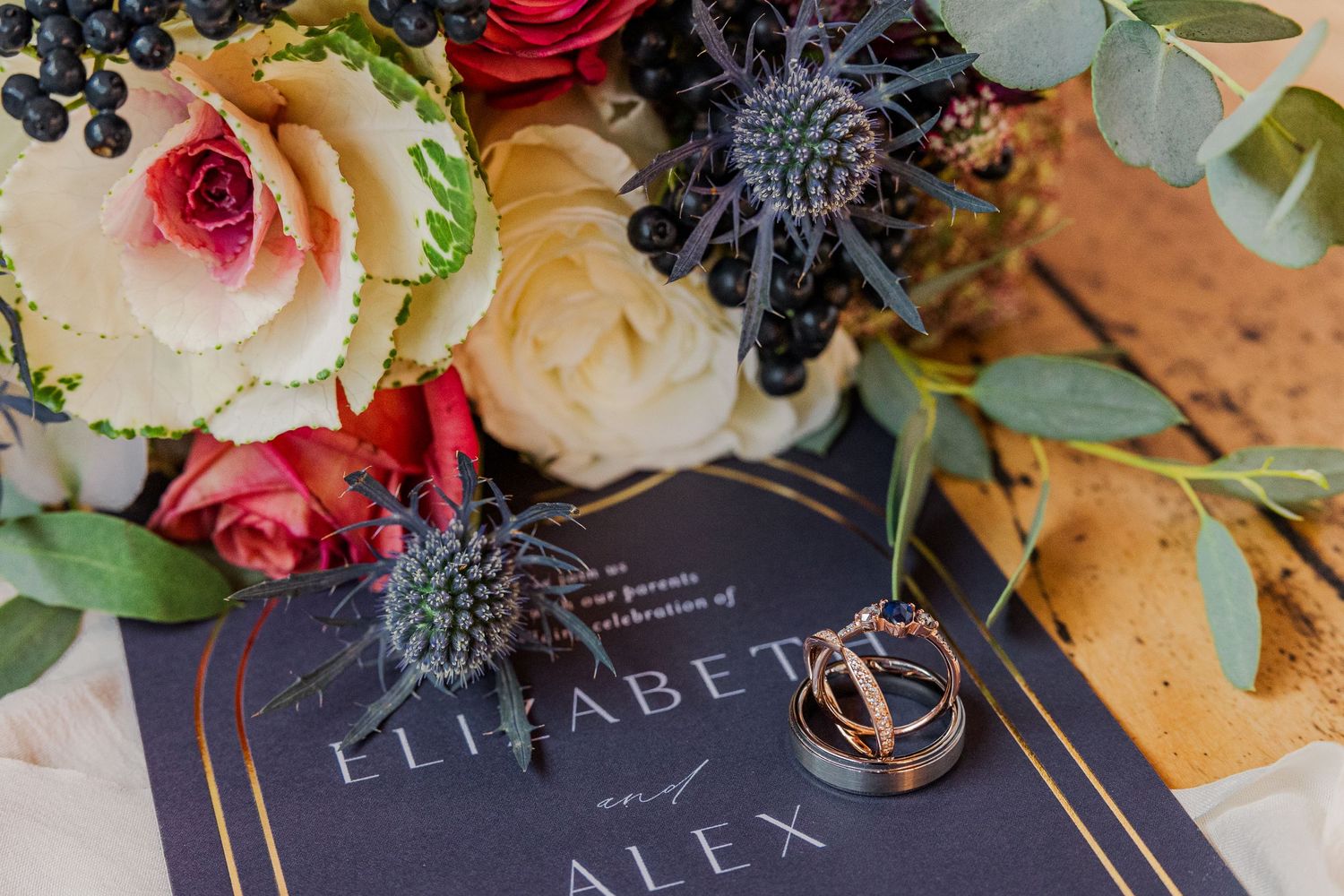 Elegant wedding stationery with roses and rings decorated with blueberries and thistle flowers.