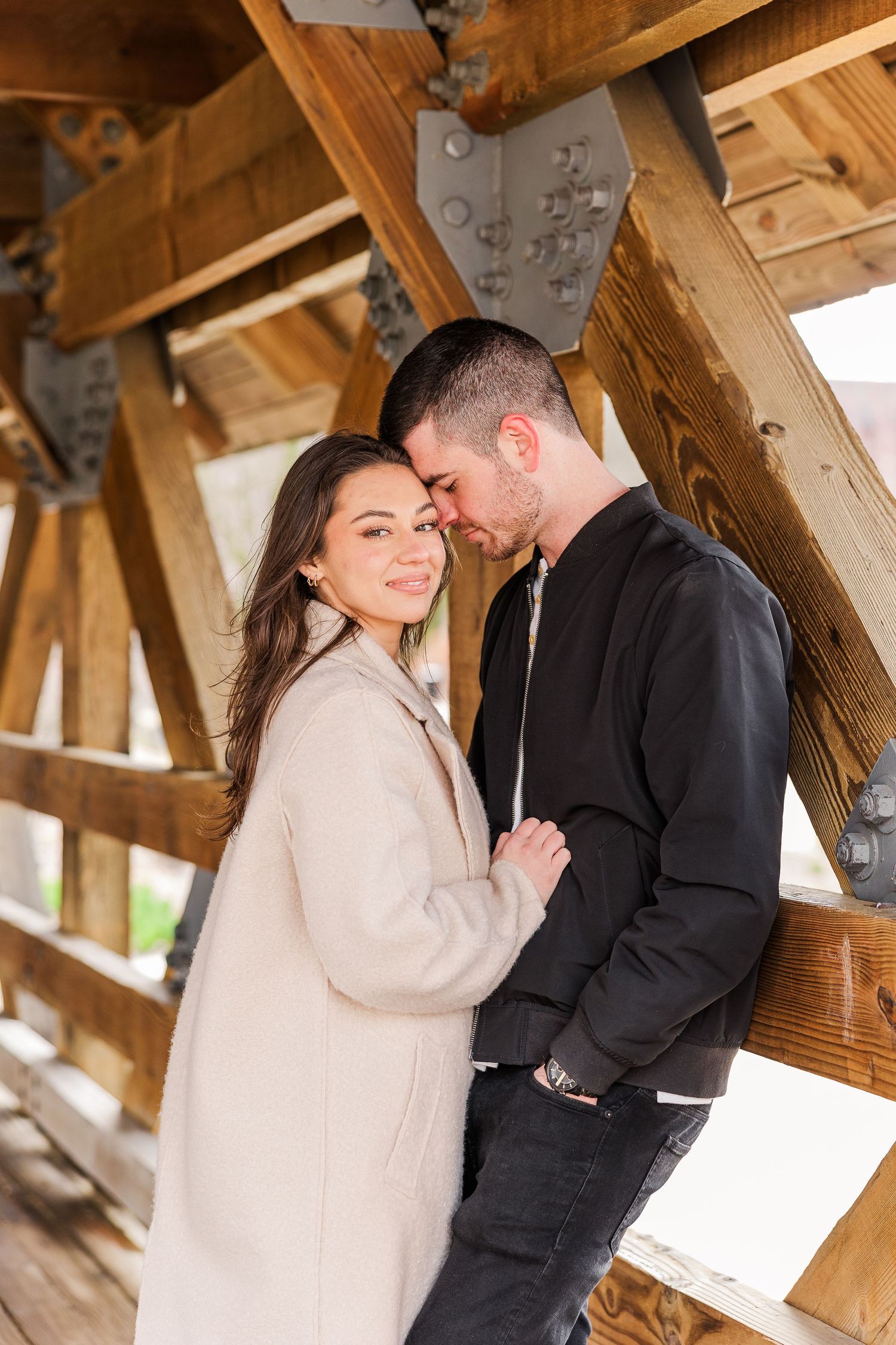 A couple shares an intimate moment while standing in a rustic wooden bridge structure.
