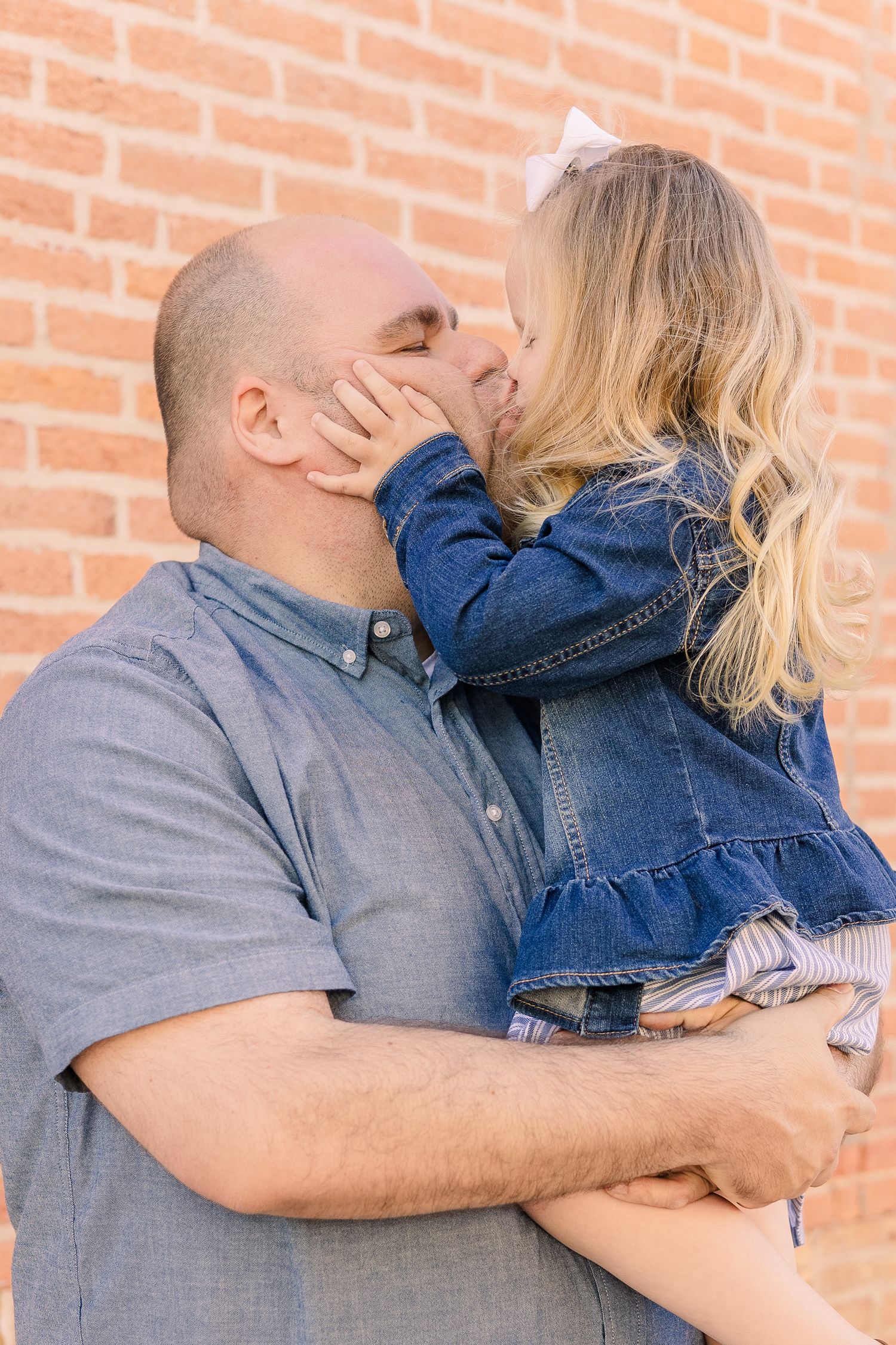 Sweet embrace between child in denim jacket and adult against brick wall.