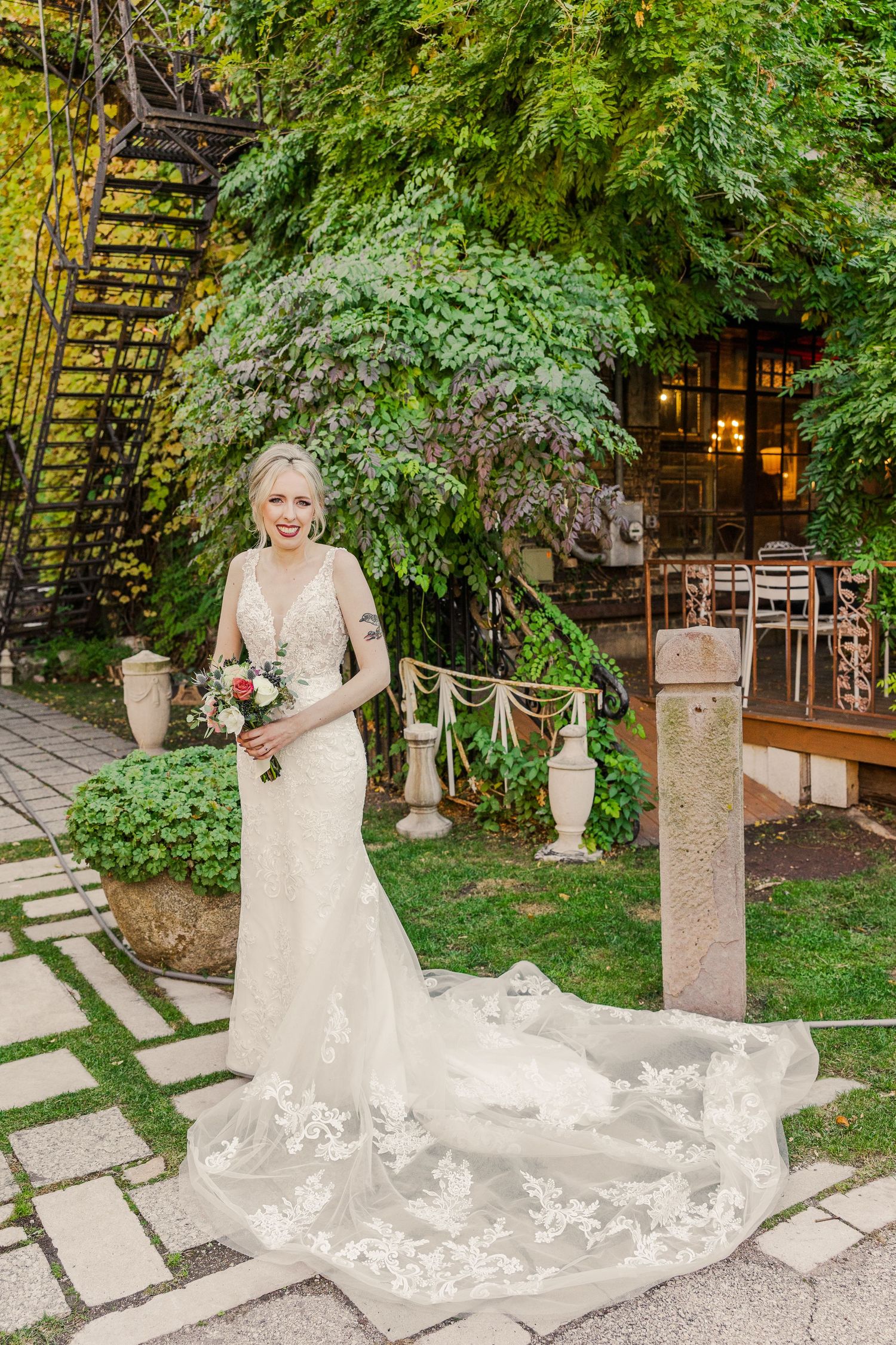 A bridal portrait in a garden setting featuring a flowing lace gown with a dramatic train.