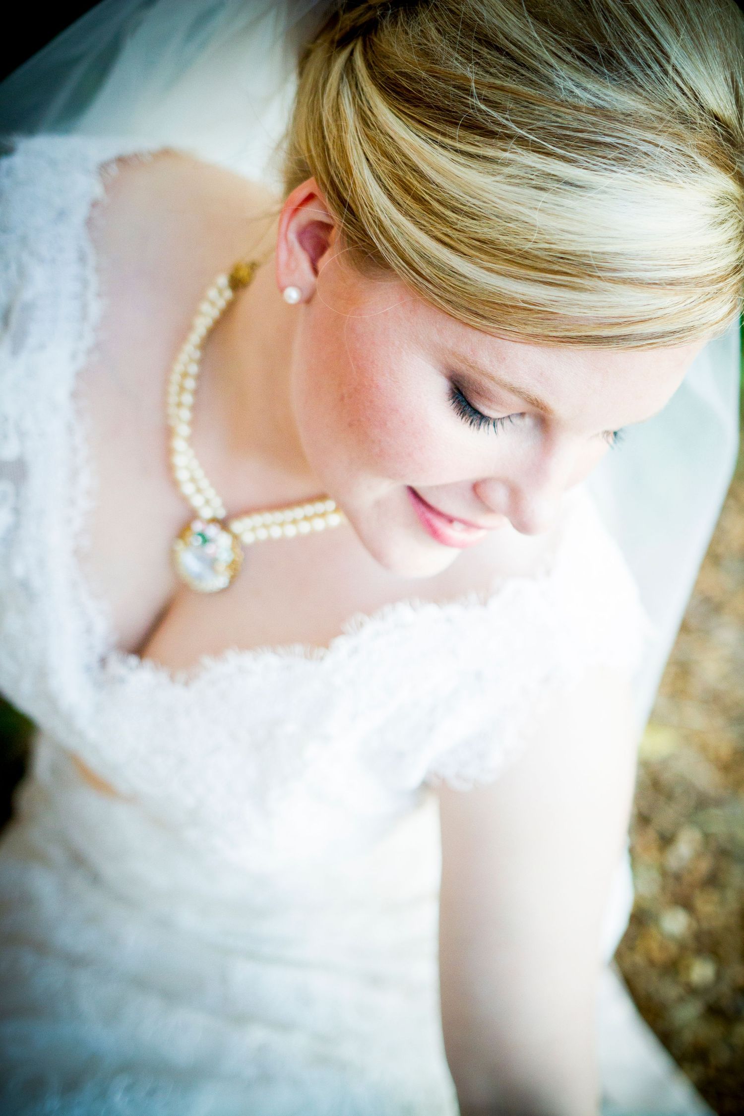 Close up bridal portrait showing delicate pearl necklace and lace dress details.
