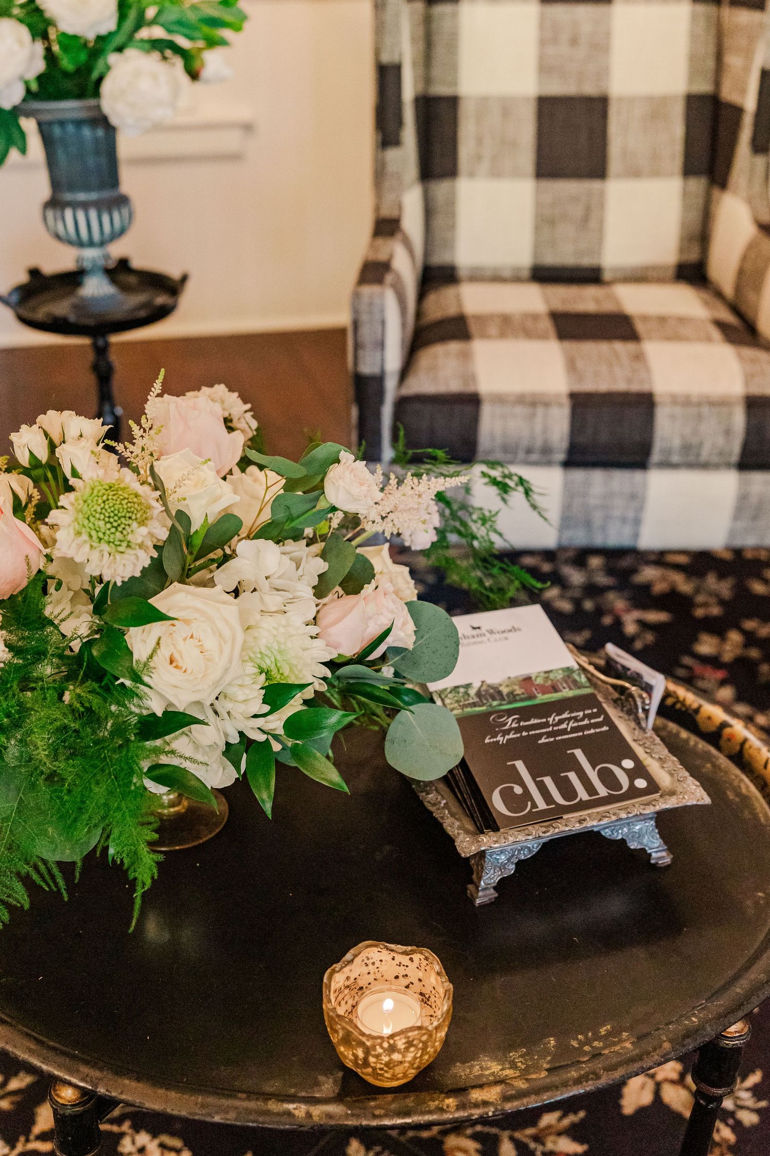 Elegant coffee table setting with white floral arrangement, candle holder and black and white plaid chair.