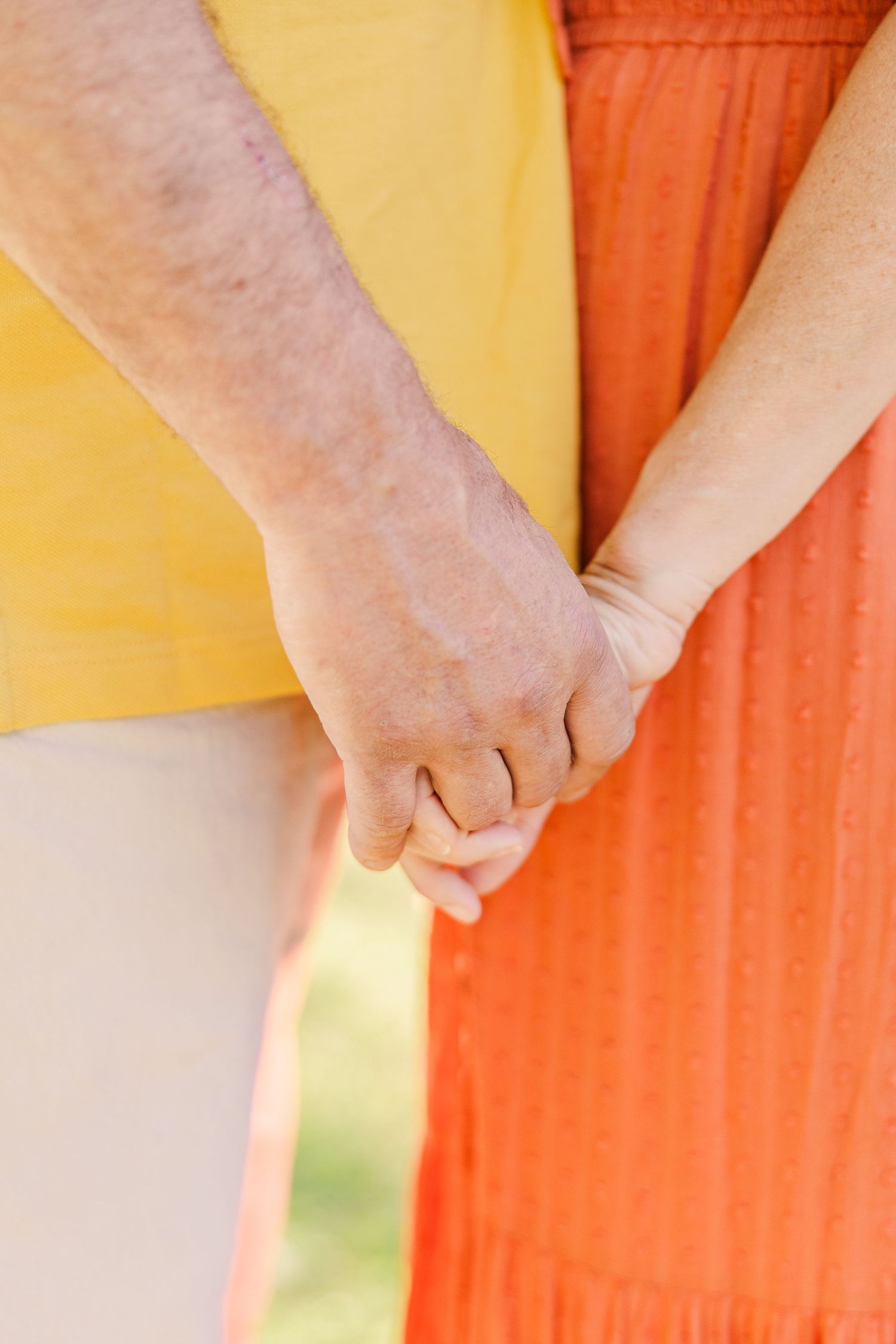 Close-up of two people holding hands wearing yellow and orange clothing.