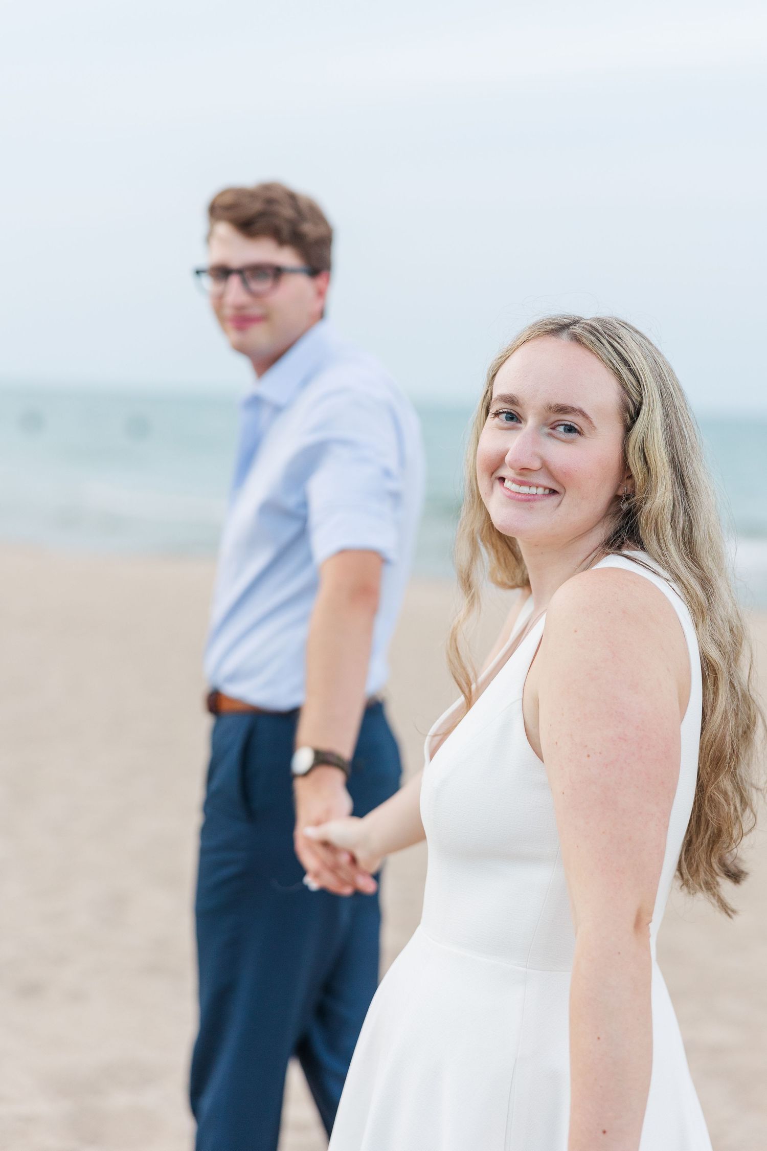 Elizabeth and Joe walkin hand-in-hand along North Avenue Beach, with gentle waves and a soft sunset in the background
