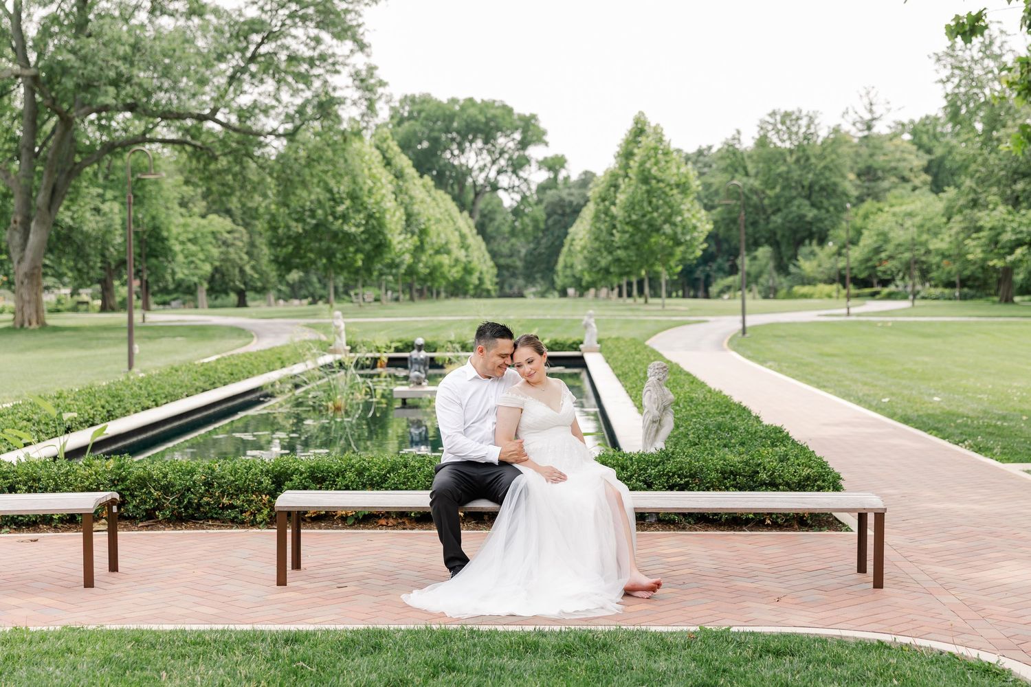 Wide portrait of the newlyweds sitting together on a bench surrounded by Cantigny Park’s formal gardens.