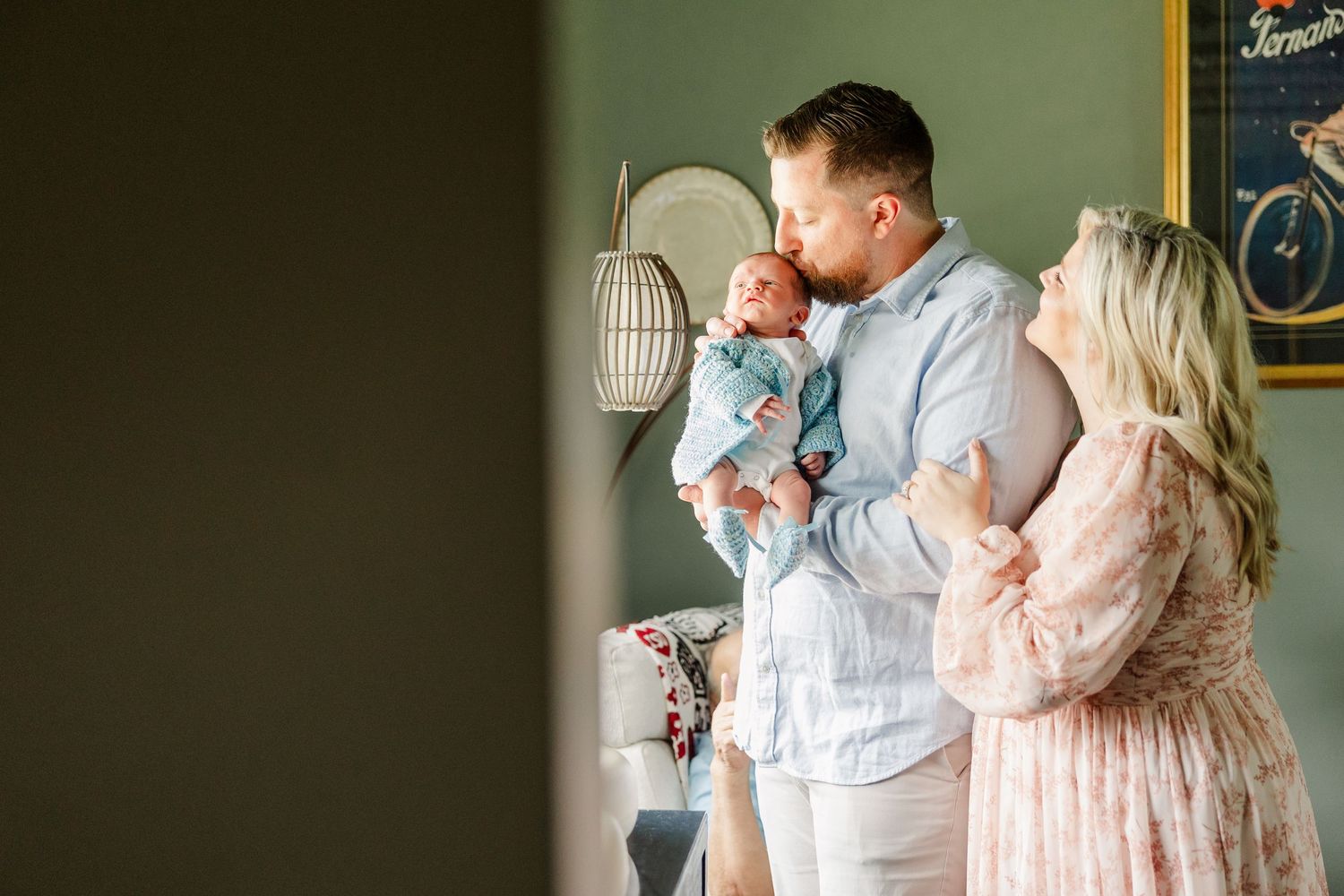 New parents sharing tender moment with newborn baby in softly lit green nursery room.