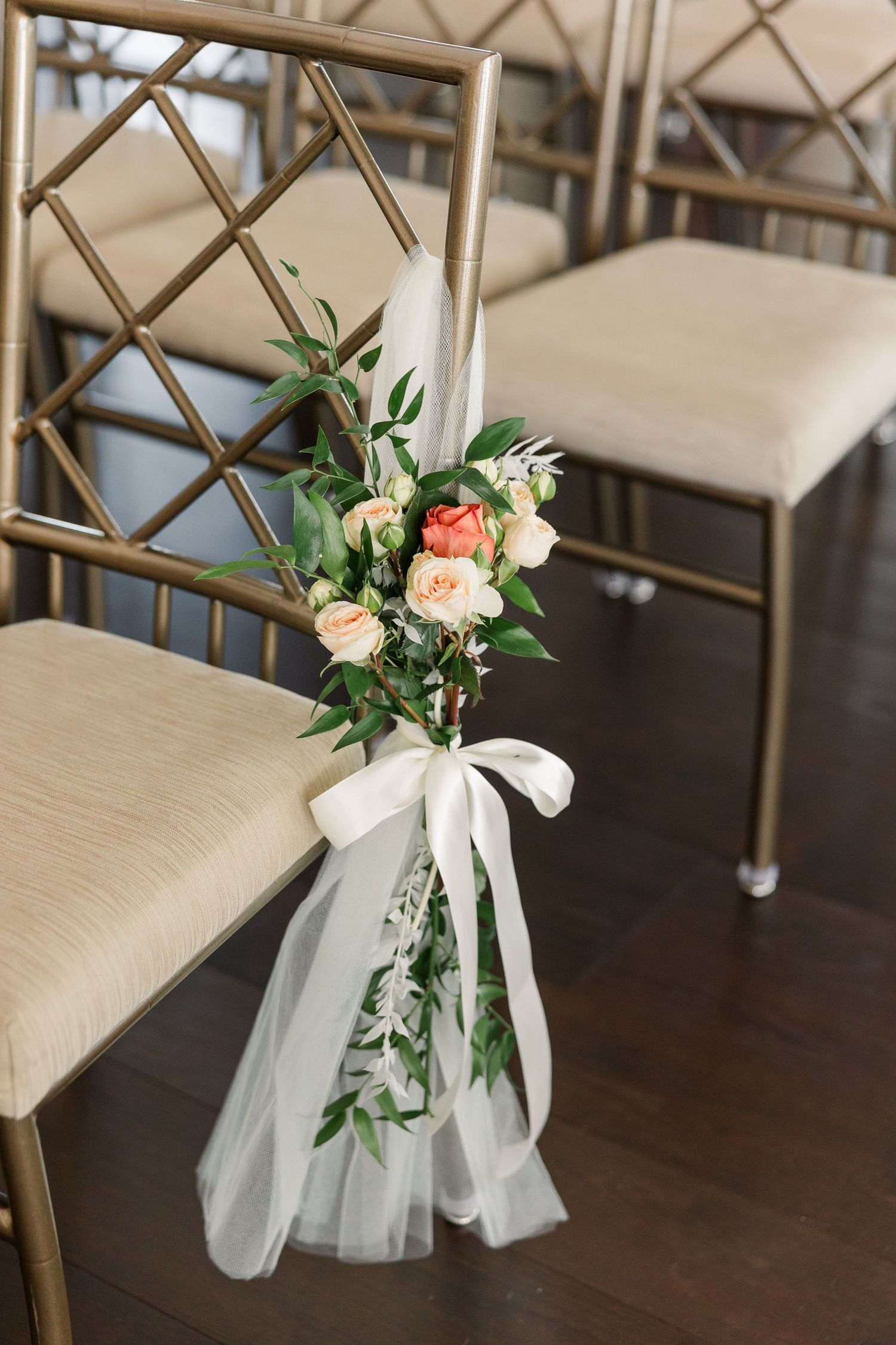 Gold wedding ceremony chair decorated with a small bouquet of peach roses, greenery, white ribbon, and flowing tulle.