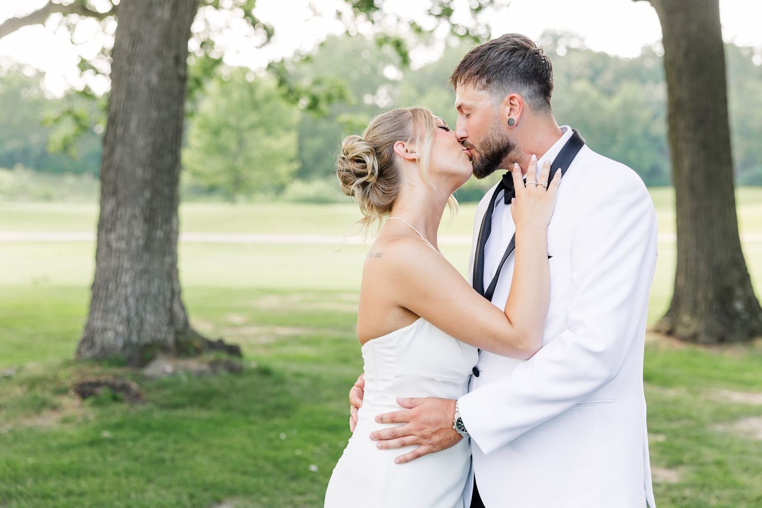 Bride and groom sharing romantic kiss outdoors under trees in wedding attire.