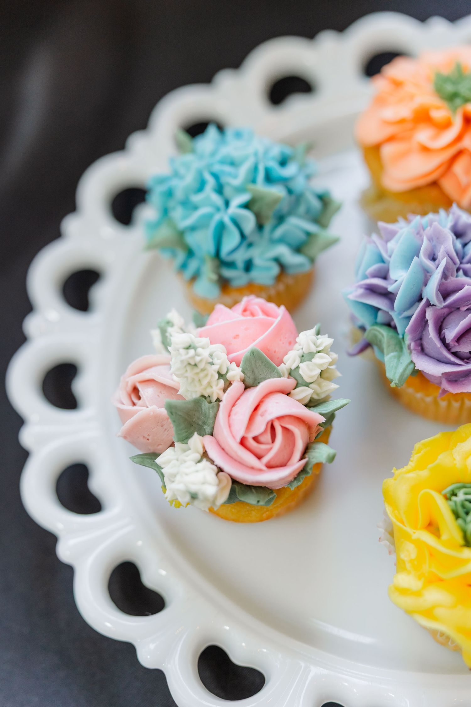 Wildflower-frosted cupcakes on scalloped white cake stand at bridal shower