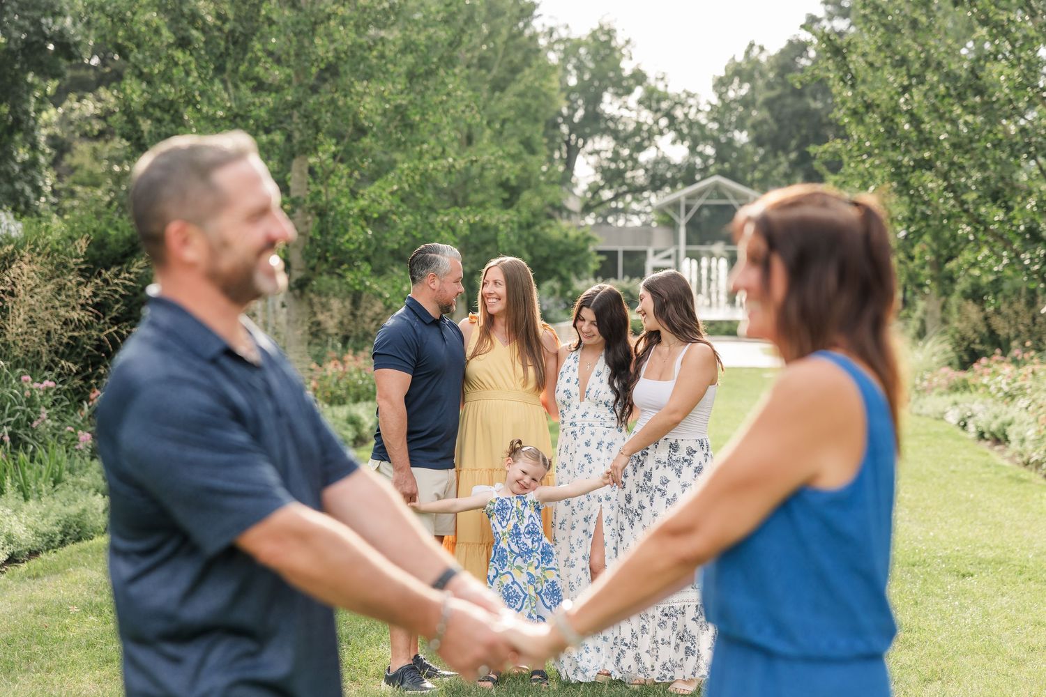 Family holding hands in a lush garden, with children and adults in colorful outfits during an outdoor photo session.