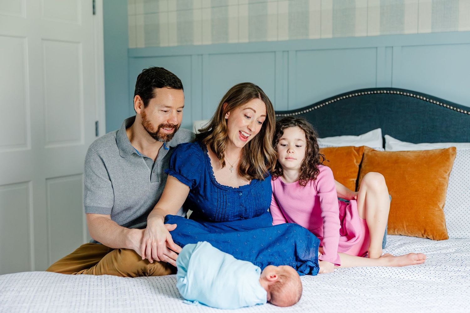 Parents and daughter with newborn on bed during lifestyle newborn session in Crystal Lake, Illinois