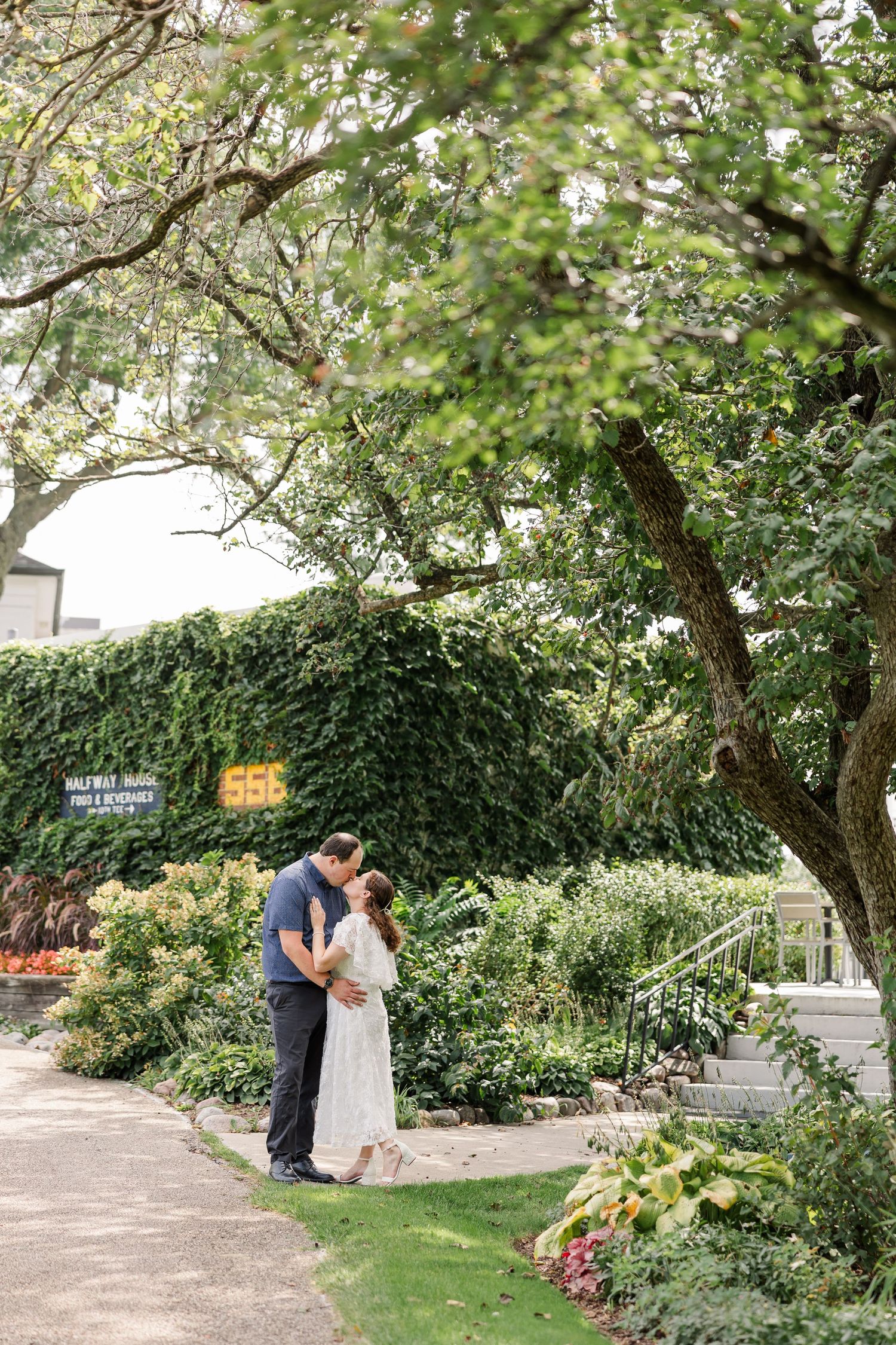 Couple sharing a tender embrace in a lush garden with ivy-covered walls and blooming flower beds.