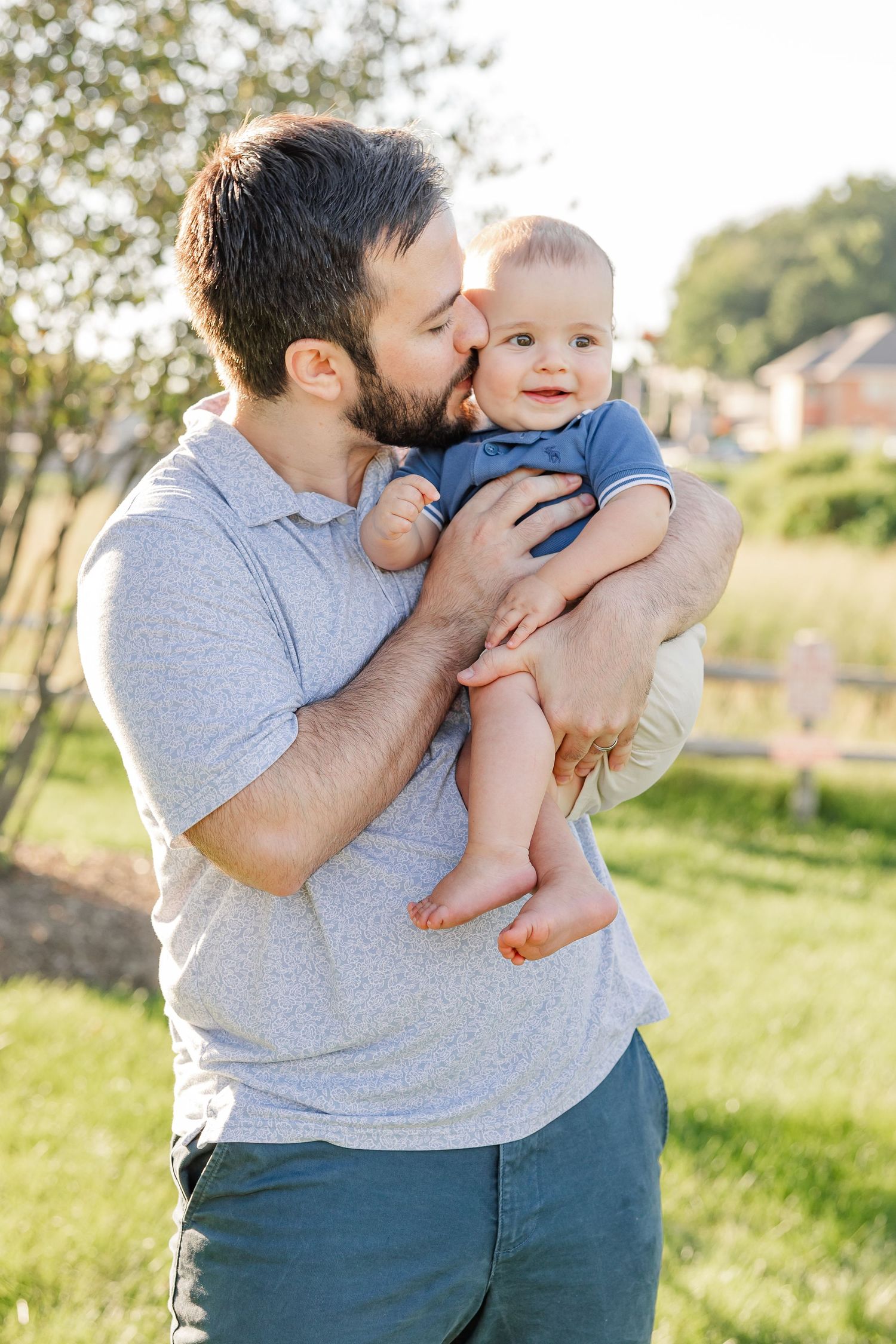 Loving bearded father kissing infant baby on the head while holding them in a sunny outdoor park.
