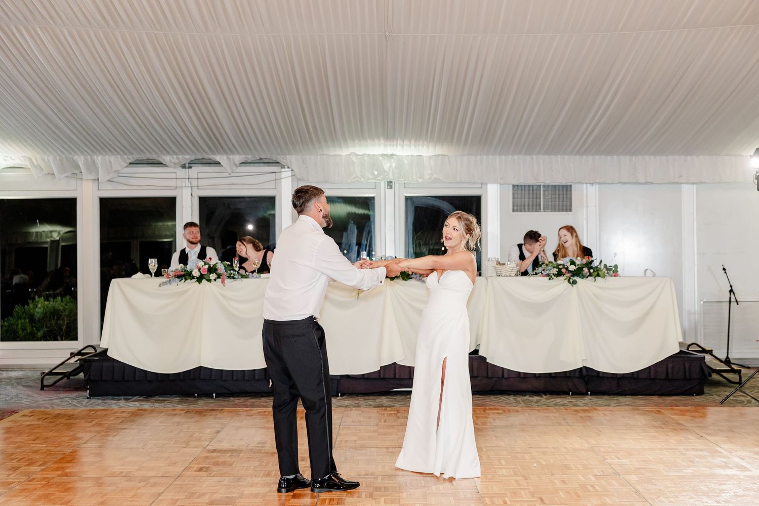 Bride and groom share first dance on wooden floor in elegant white tent wedding reception.