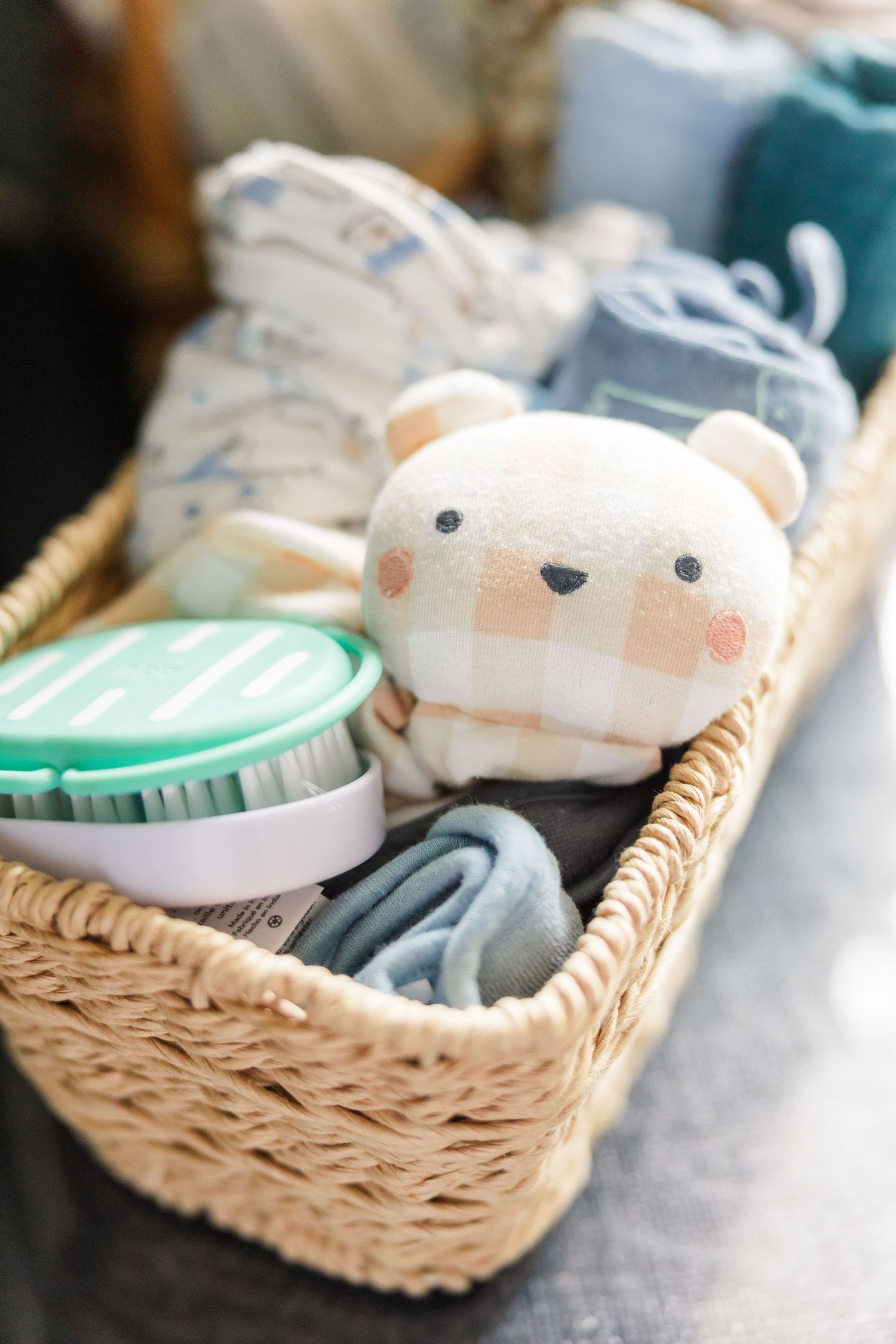A wicker basket filled with baby essentials including a plaid bear toy, wipes, and soft blankets.