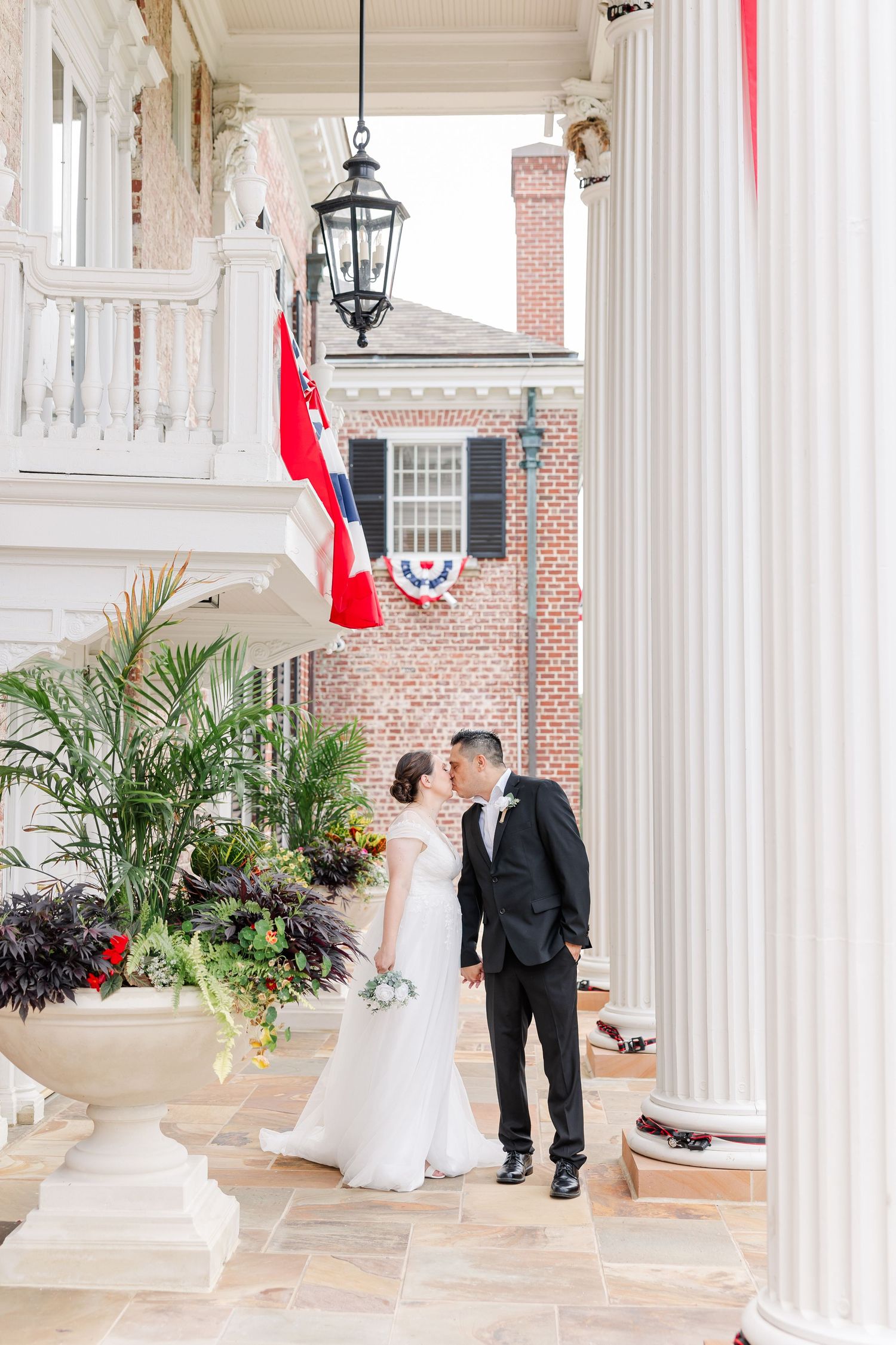 Bride and groom posing beneath the white columns and hanging lantern at McCormick House.