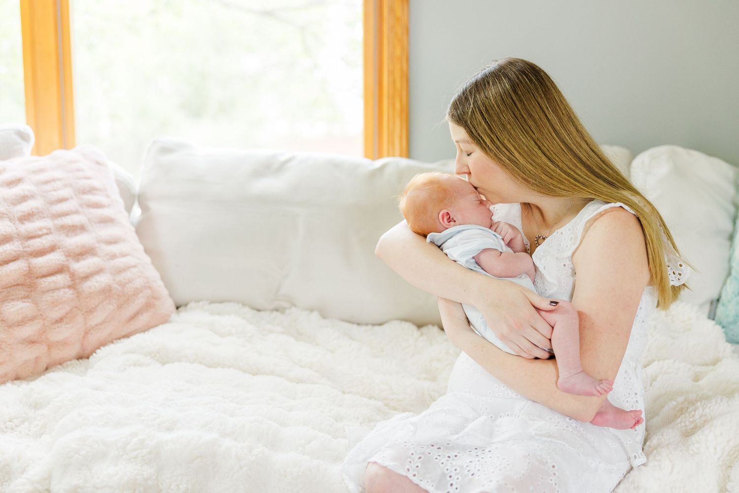 Mother kissing her newborn baby in soft natural window light during an in-home lifestyle newborn session in Vernon Hills IL