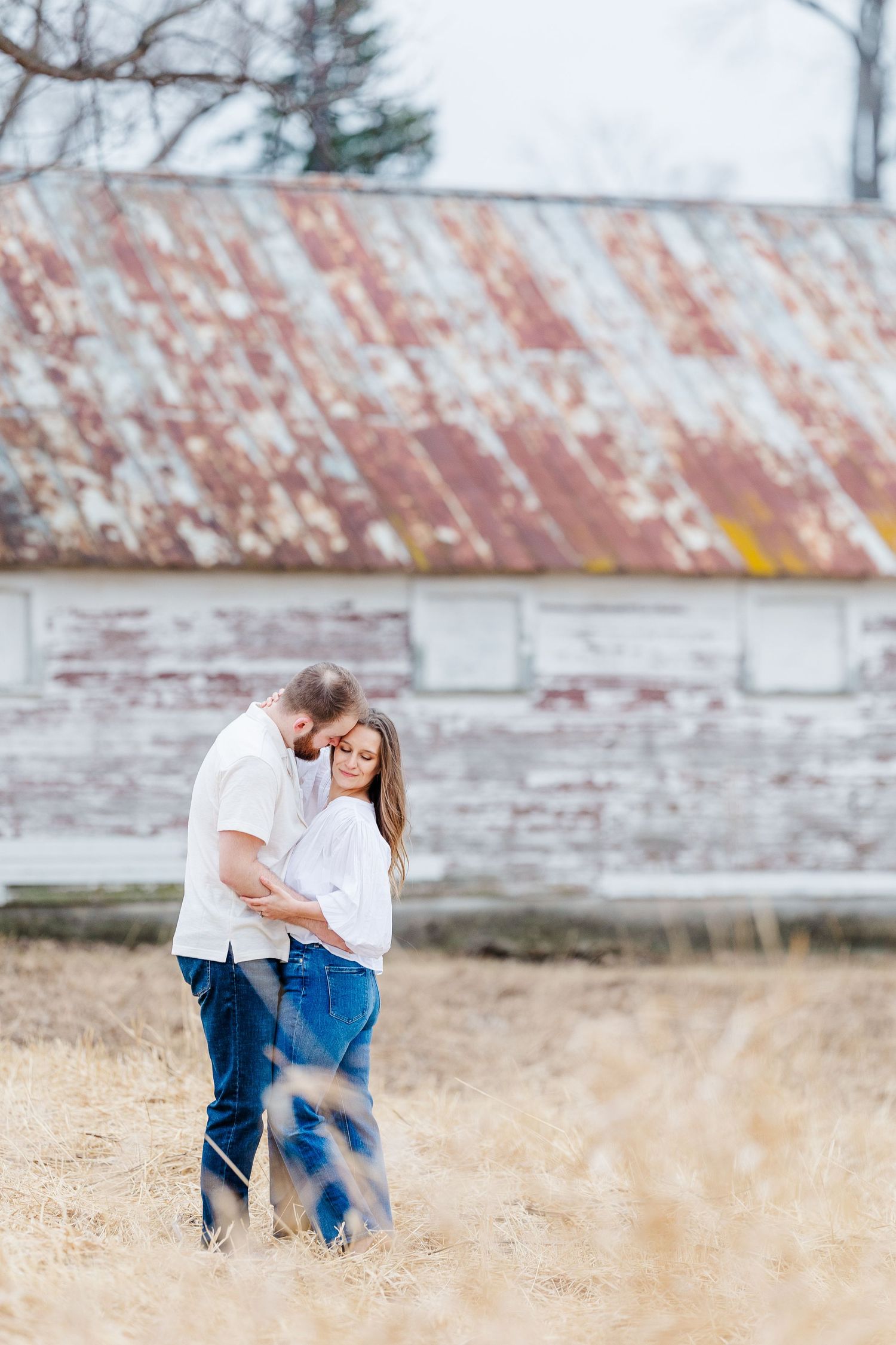 Couple kissing by rustic barn during pregnancy announcement photos in Cary, Illinois