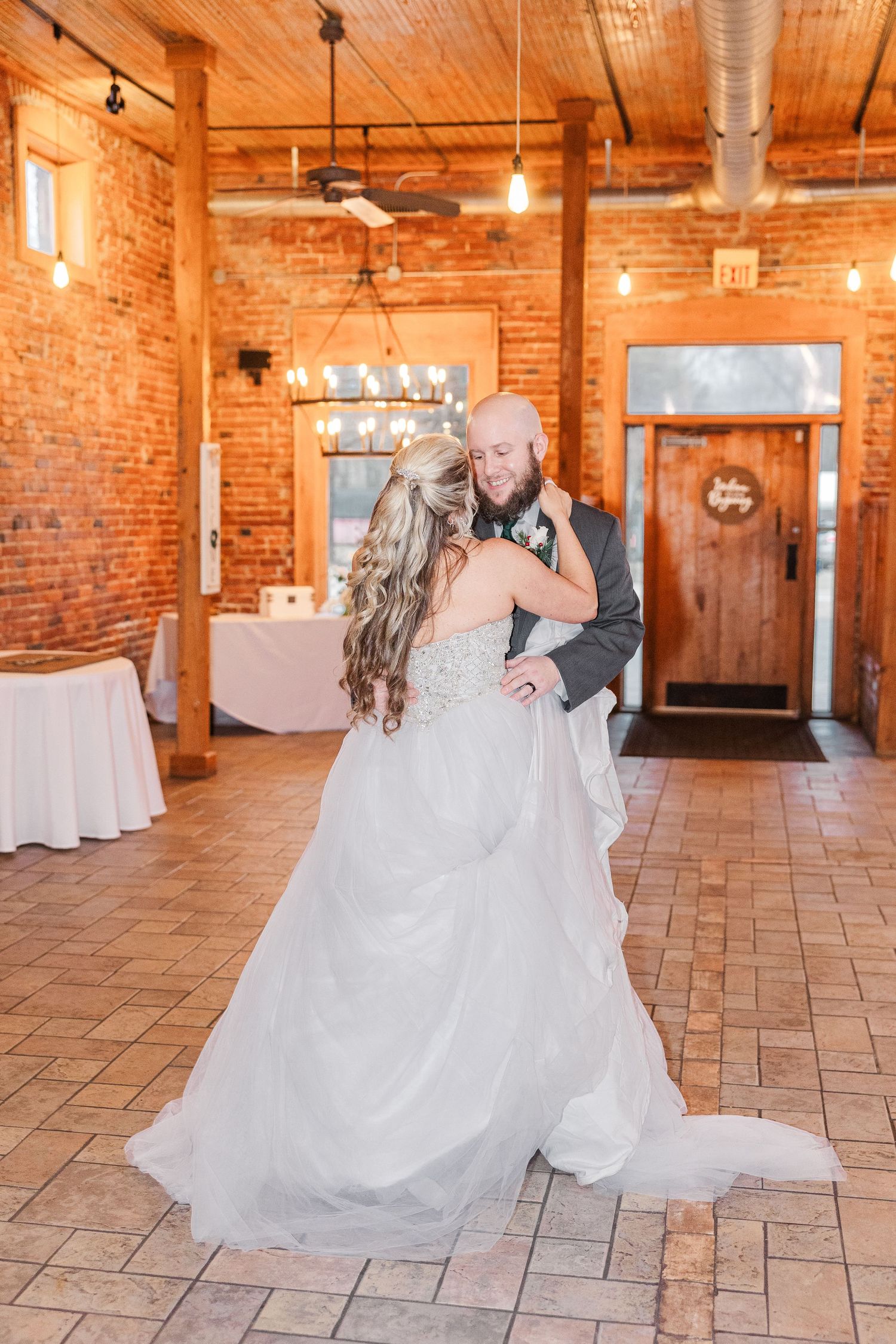 Wedding dance in rustic venue with exposed brick walls and wooden ceiling.