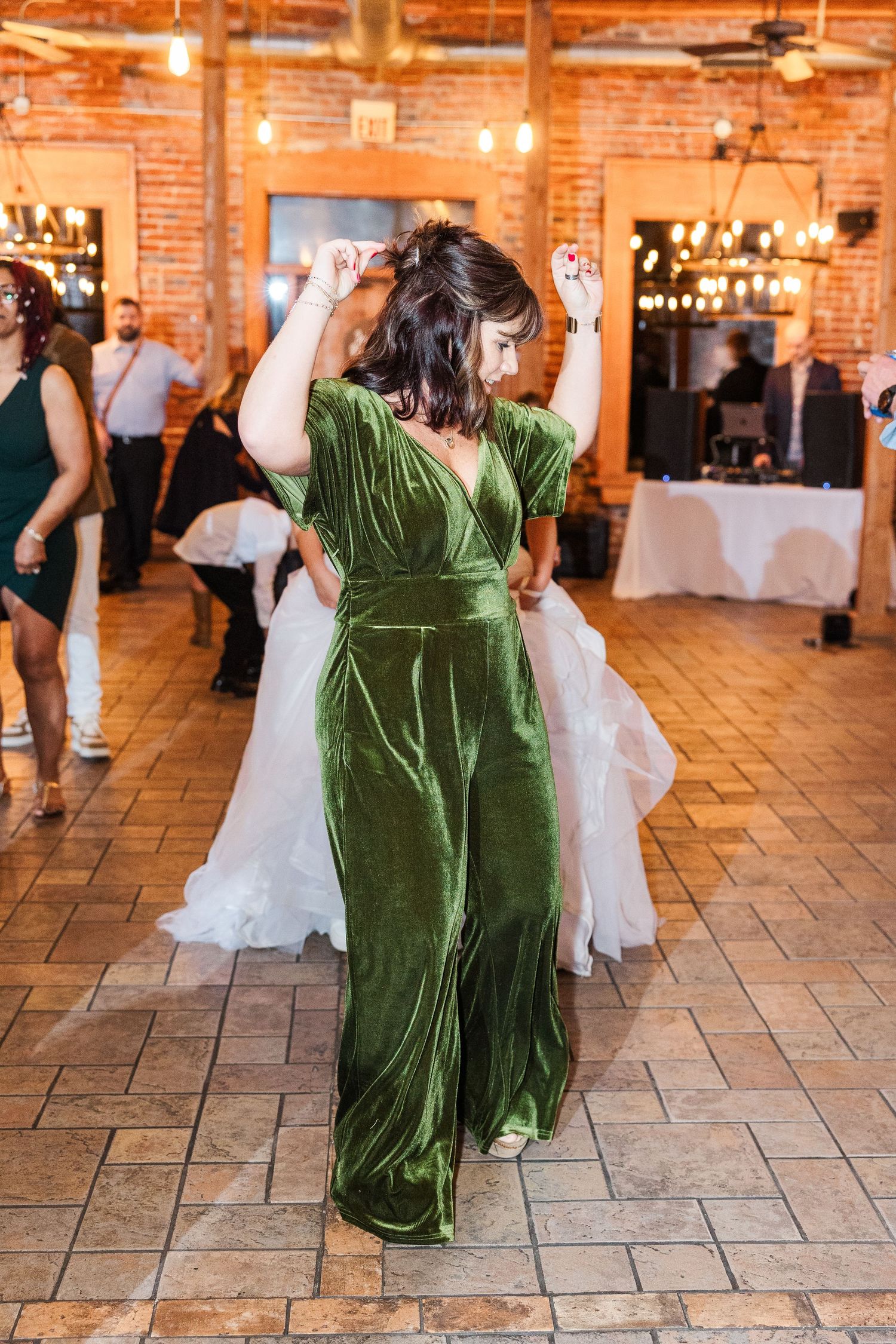 Woman in emerald velvet dress dancing at a rustic venue with brick walls.