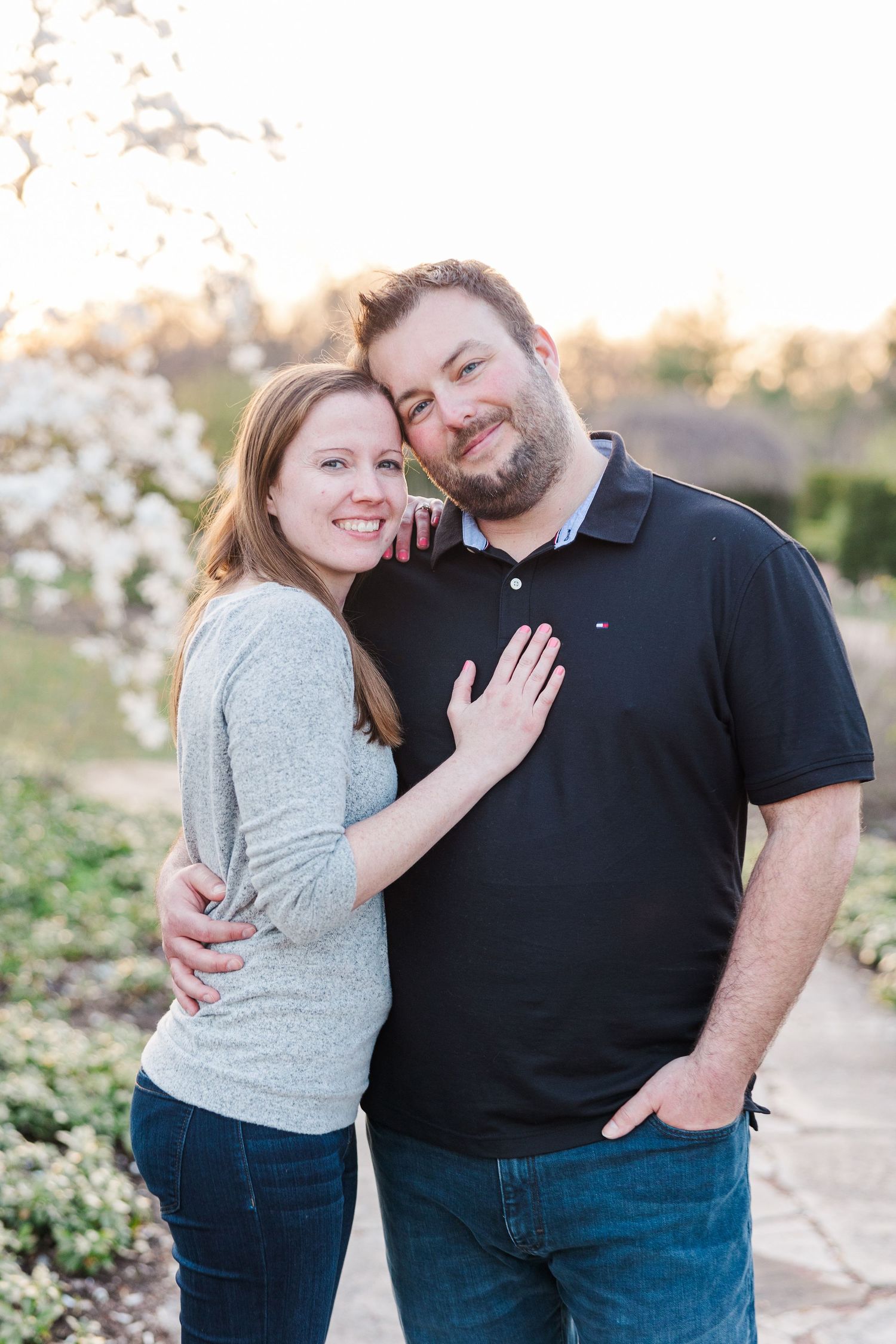 Romantic couple embracing outdoors in a garden setting during golden hour with blooming flowers in background.