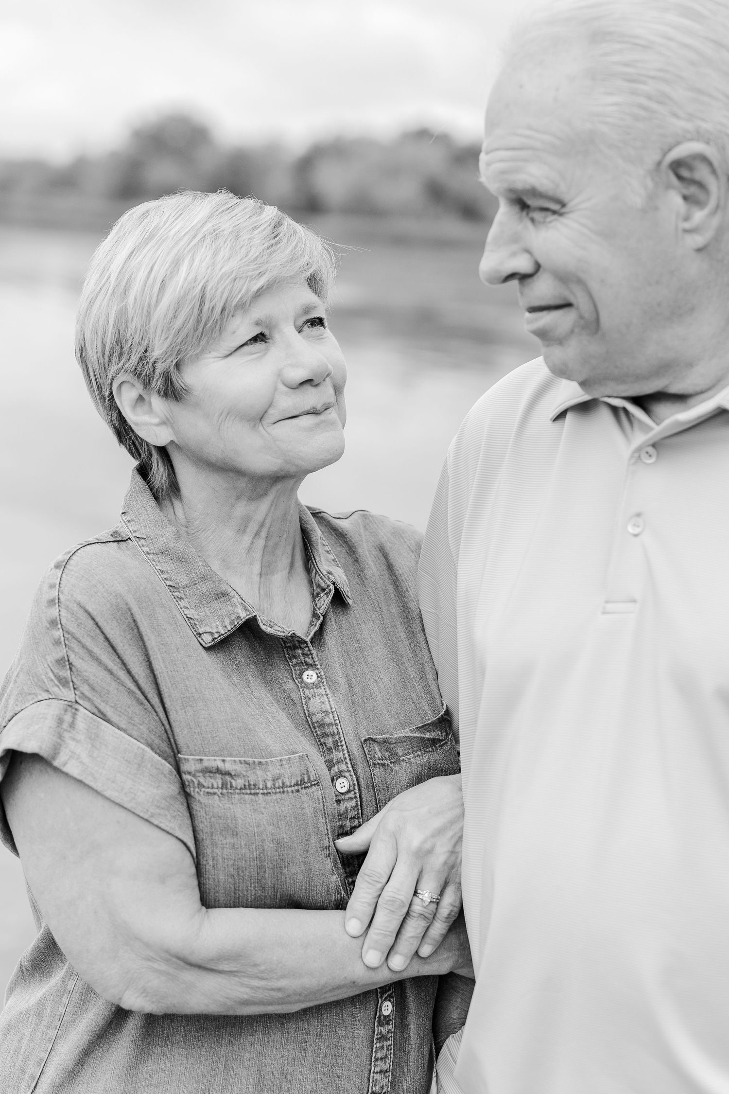 Black and white portrait of a couple in casual attire sharing a tender moment outdoors.